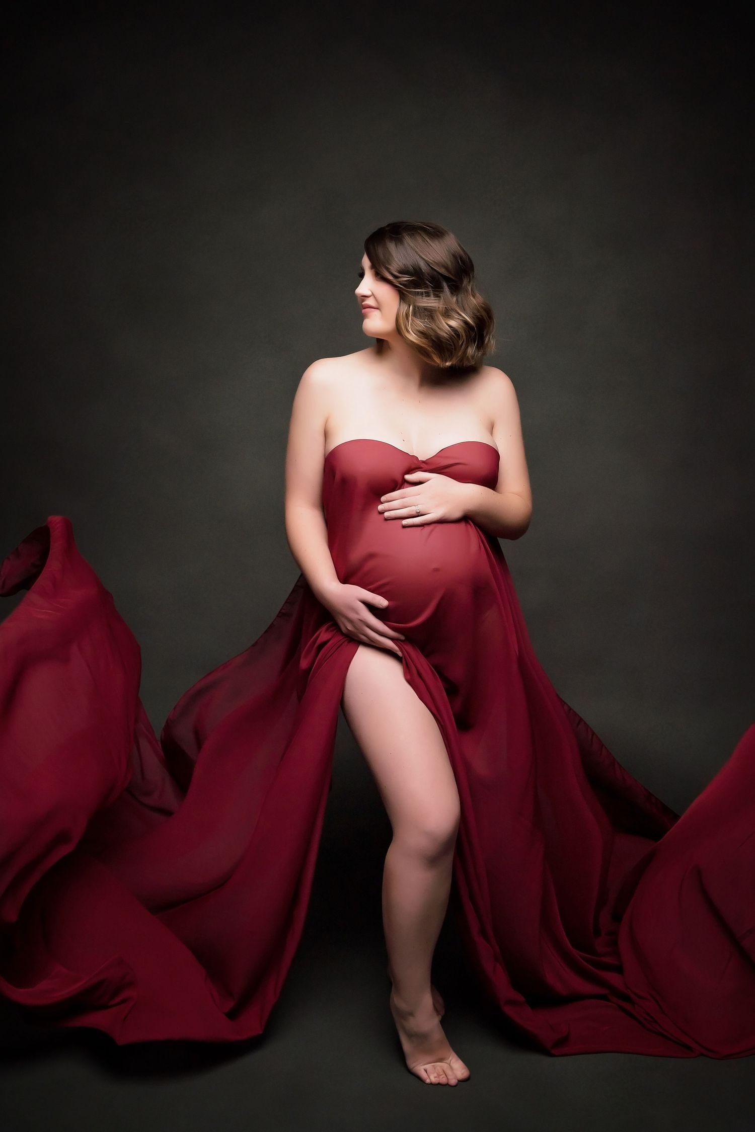 Maternity portrait with deep red fabric draping against dark studio backdrop