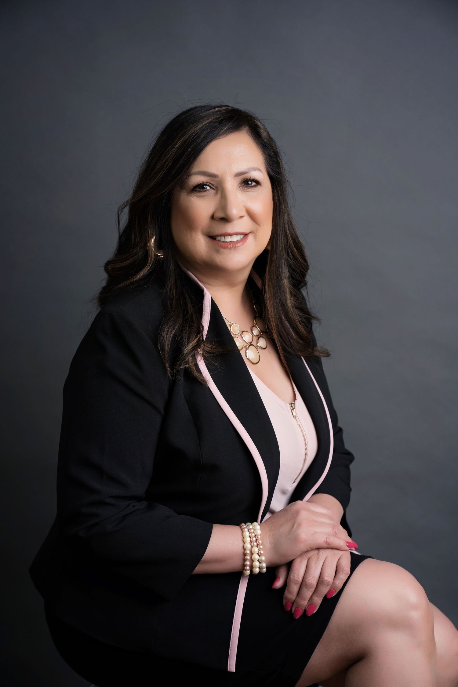 Professional portrait of woman in black blazer posed confidently against dark studio background