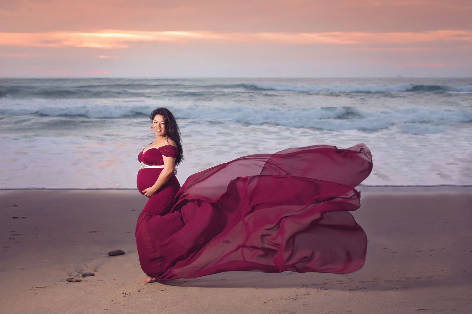Dramatic burgundy dress flowing in the wind during beach maternity session at sunset. San Diego Maternity Photographer