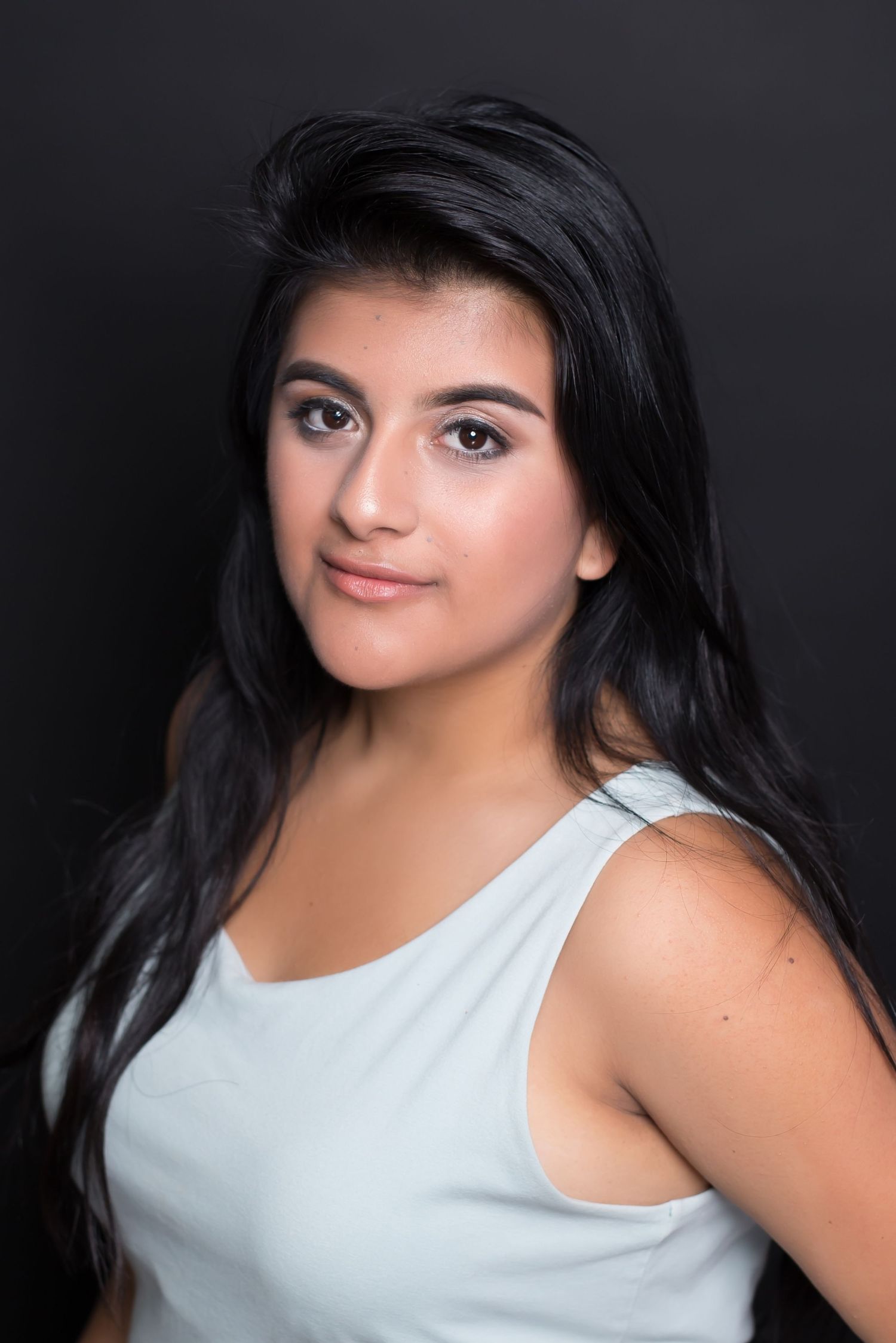 Studio headshot of woman in white tank top against solid black background