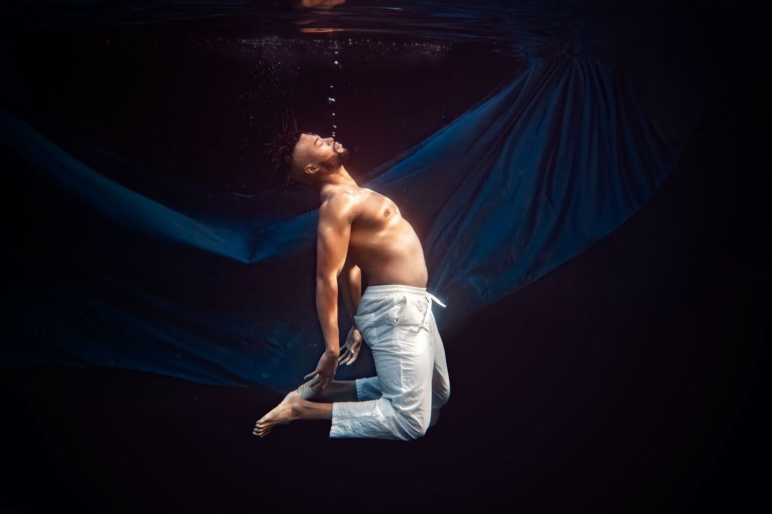 Underwater maternity portrait with blue fabric drifting gracefully in dark water