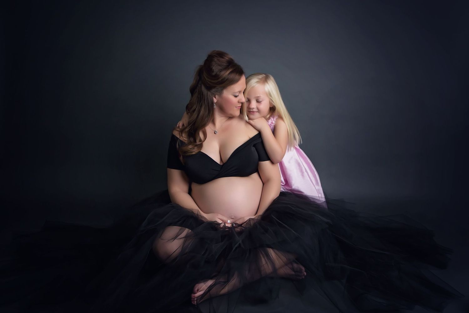 Intimate maternity portrait with black tulle dress against dark background.