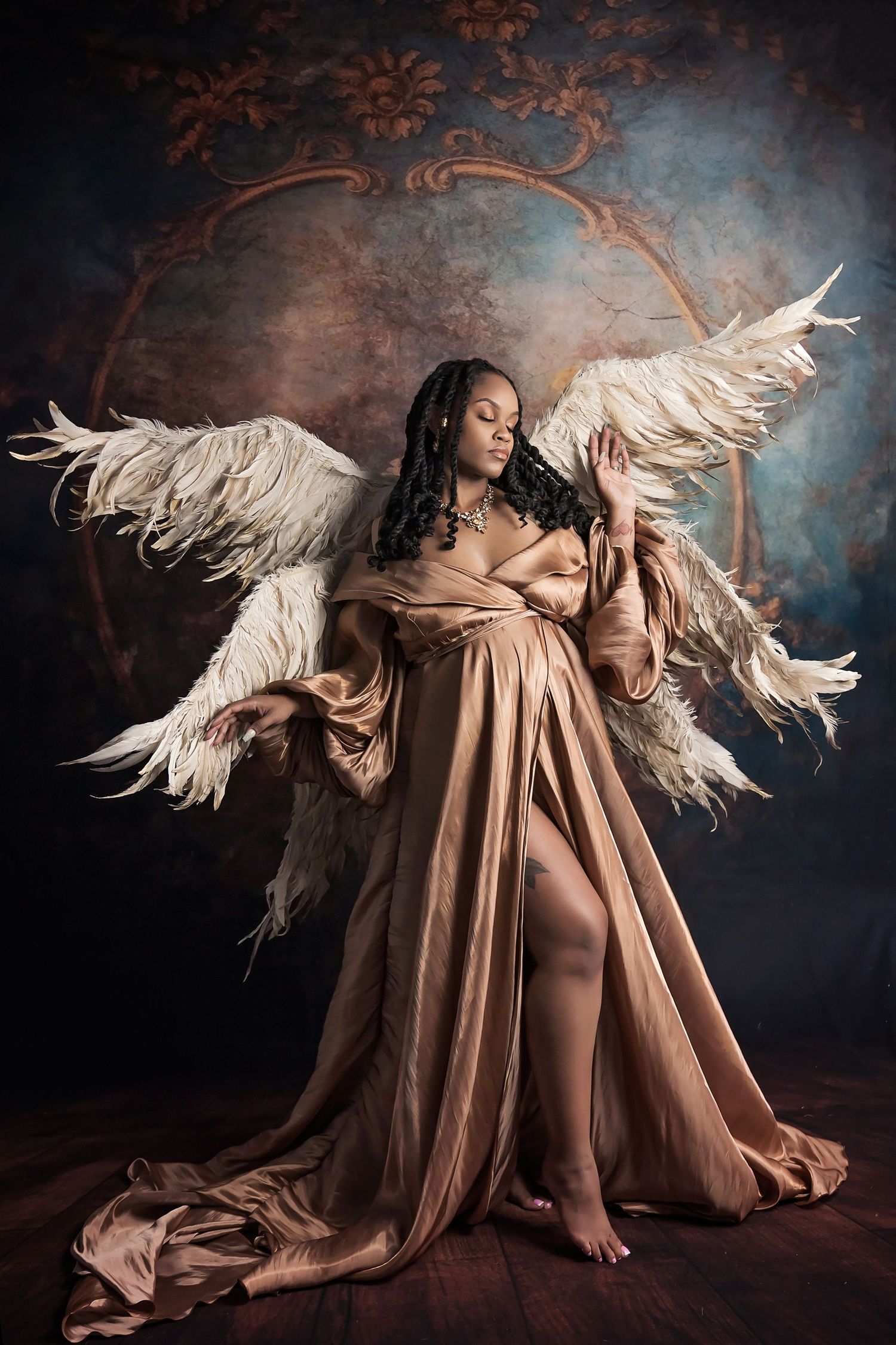 Angelic maternity portrait featuring feather wings and flowing golden gown