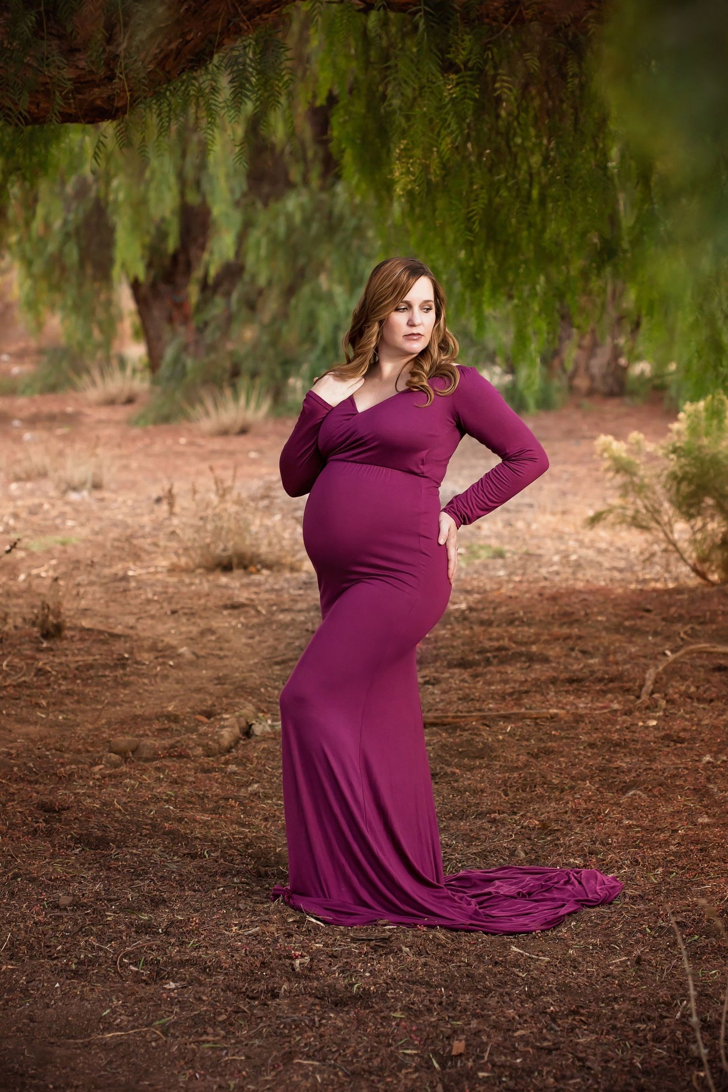 Maternity photography session showcasing a flowing burgundy dress in a rustic outdoor setting. San Diego Maternity Photographer