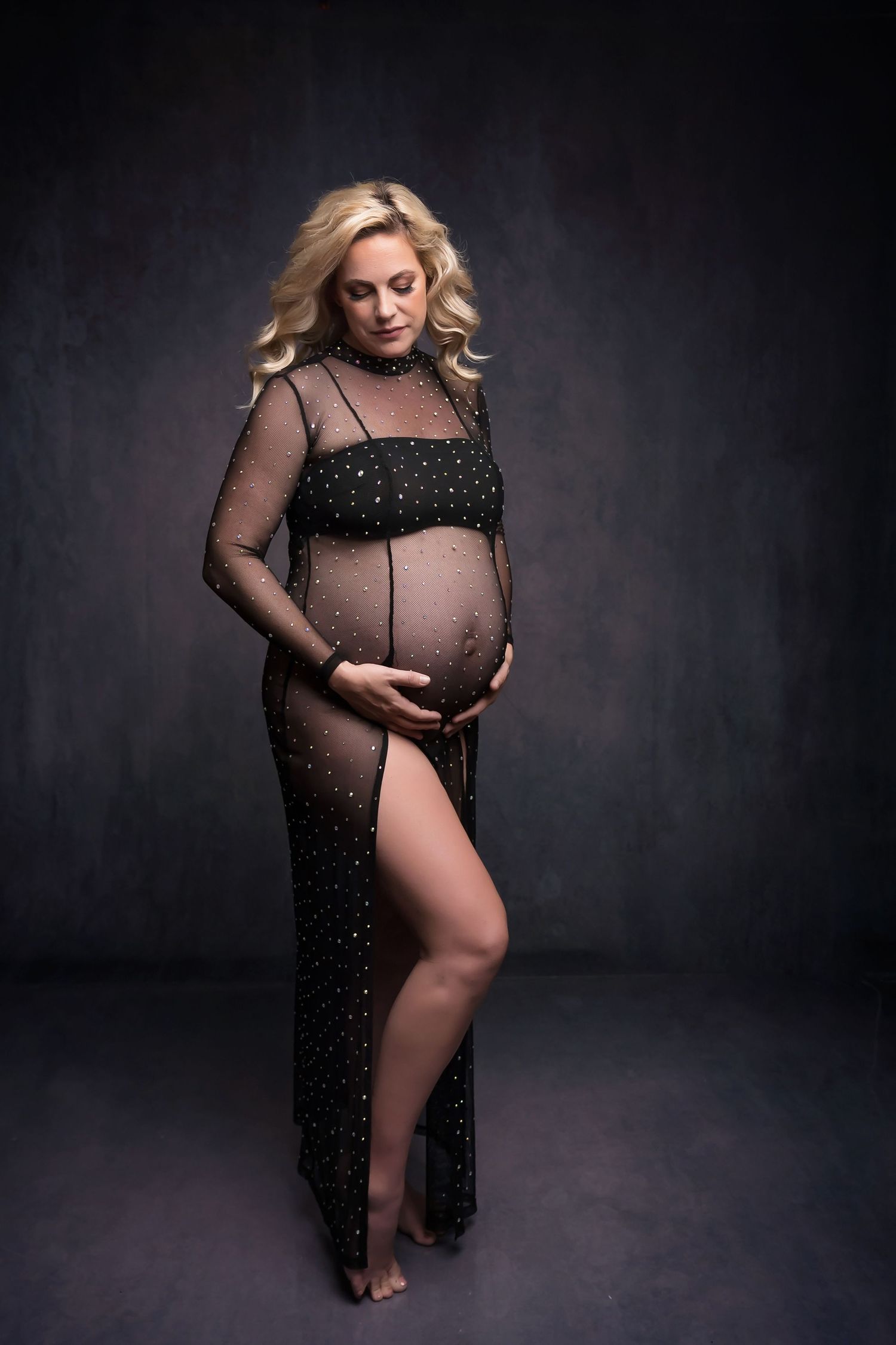 Dramatic maternity portrait in sheer black sparkly gown against dark background