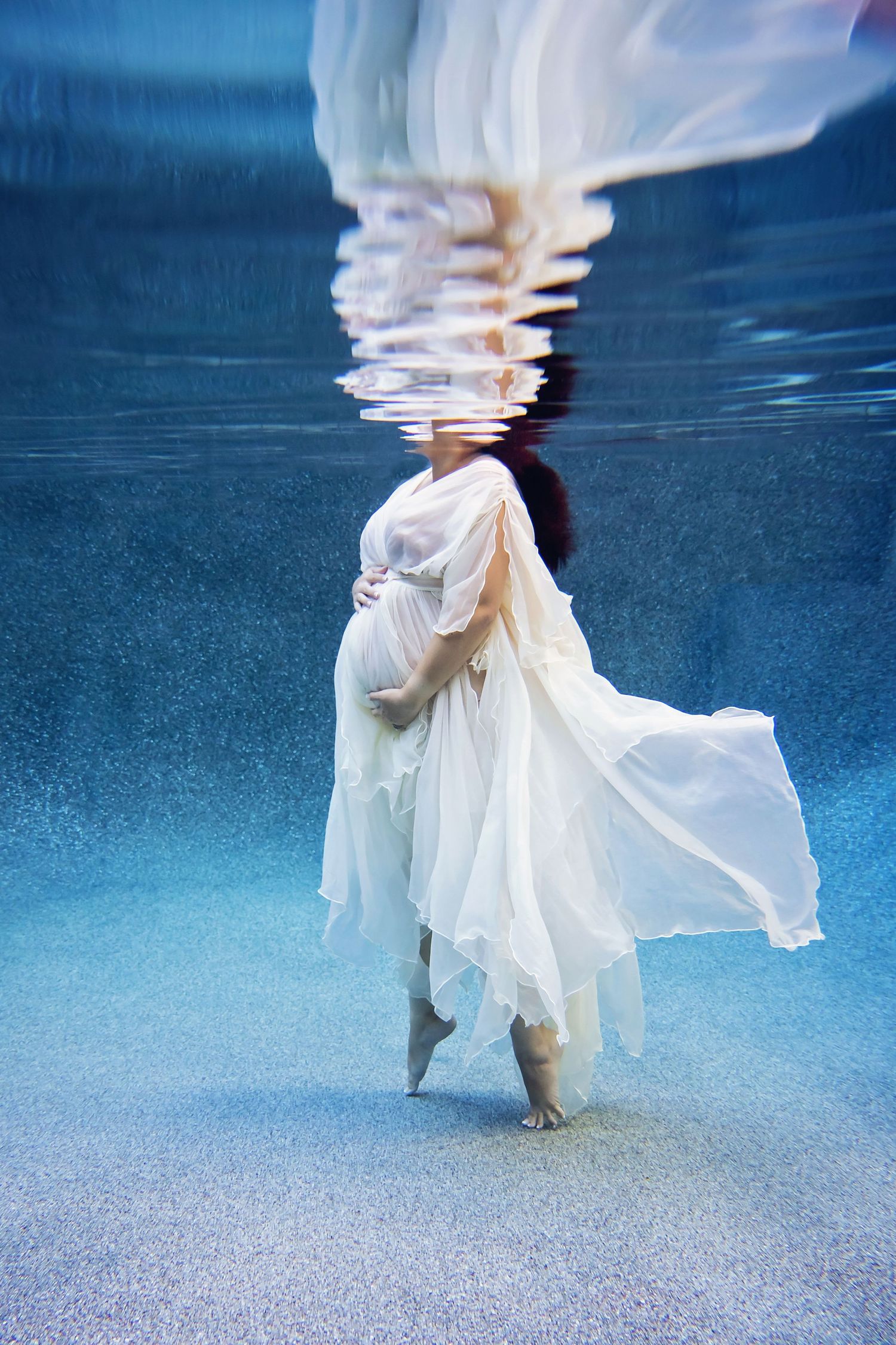 Underwater maternity portrait with white flowing gown moving softly in blue pool water — Chula Vista session