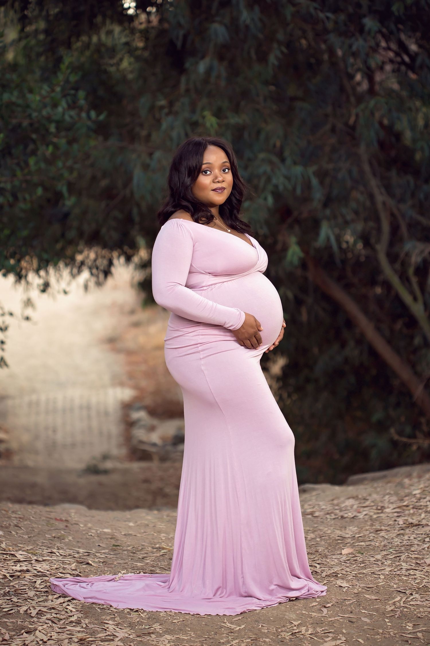 A maternity portrait session featuring a pink flowing dress against a natural outdoor setting. San Diego Maternity Photographer
