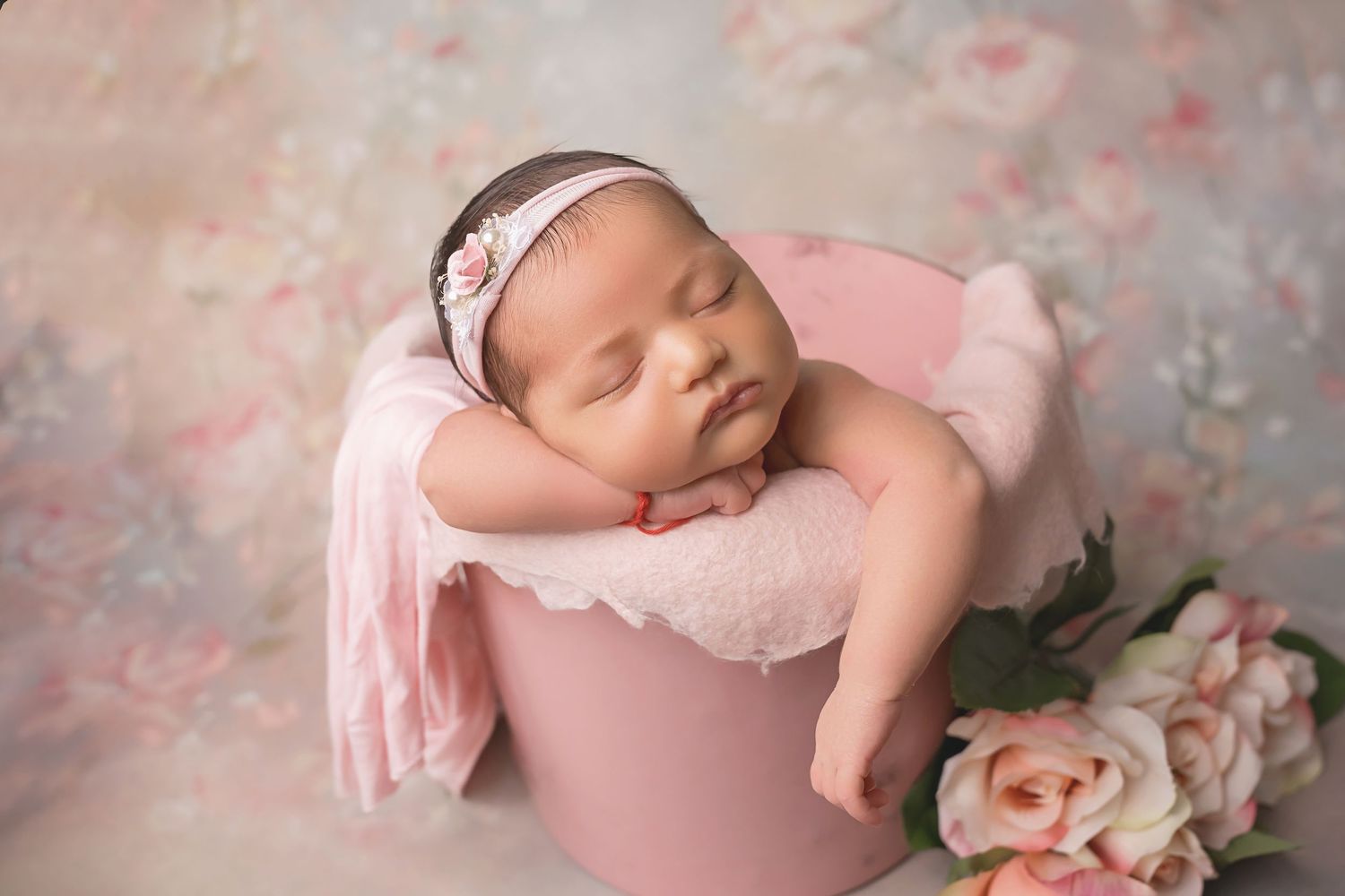 San Diego newborn photo sleeping newborn baby wearing pink while posed with delicate flowers and soft textured fabrics in a san diego studio
