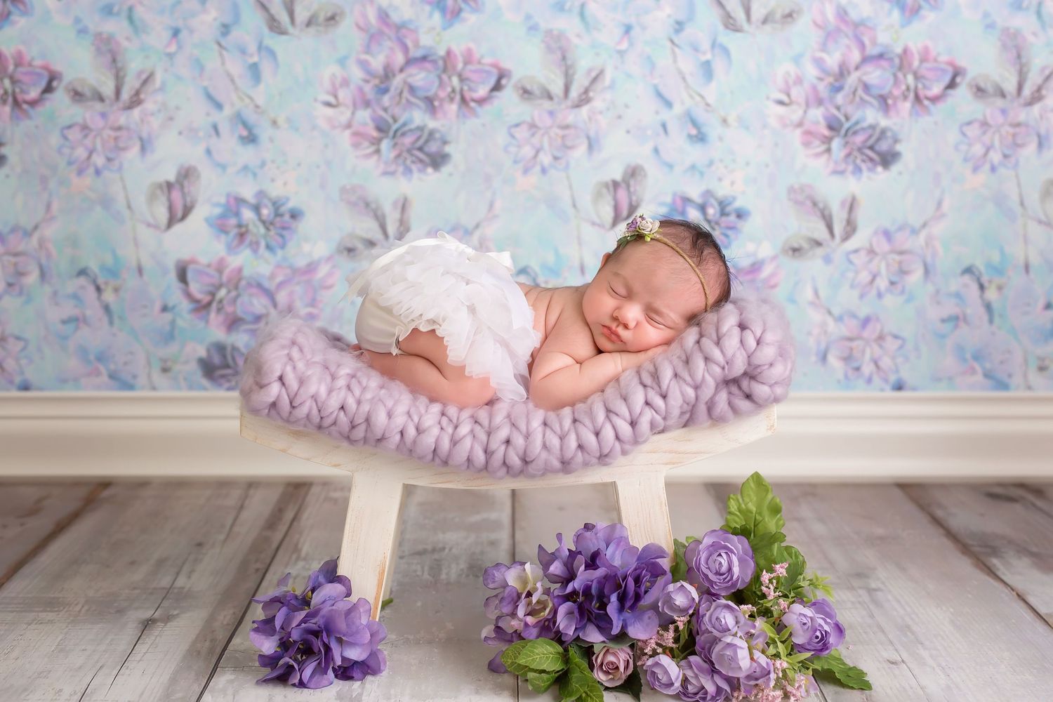 Delicate newborn photography setup with purple flowers and soft pink tulle fabric against white wooden flooring. San Diego Newborn Photograp