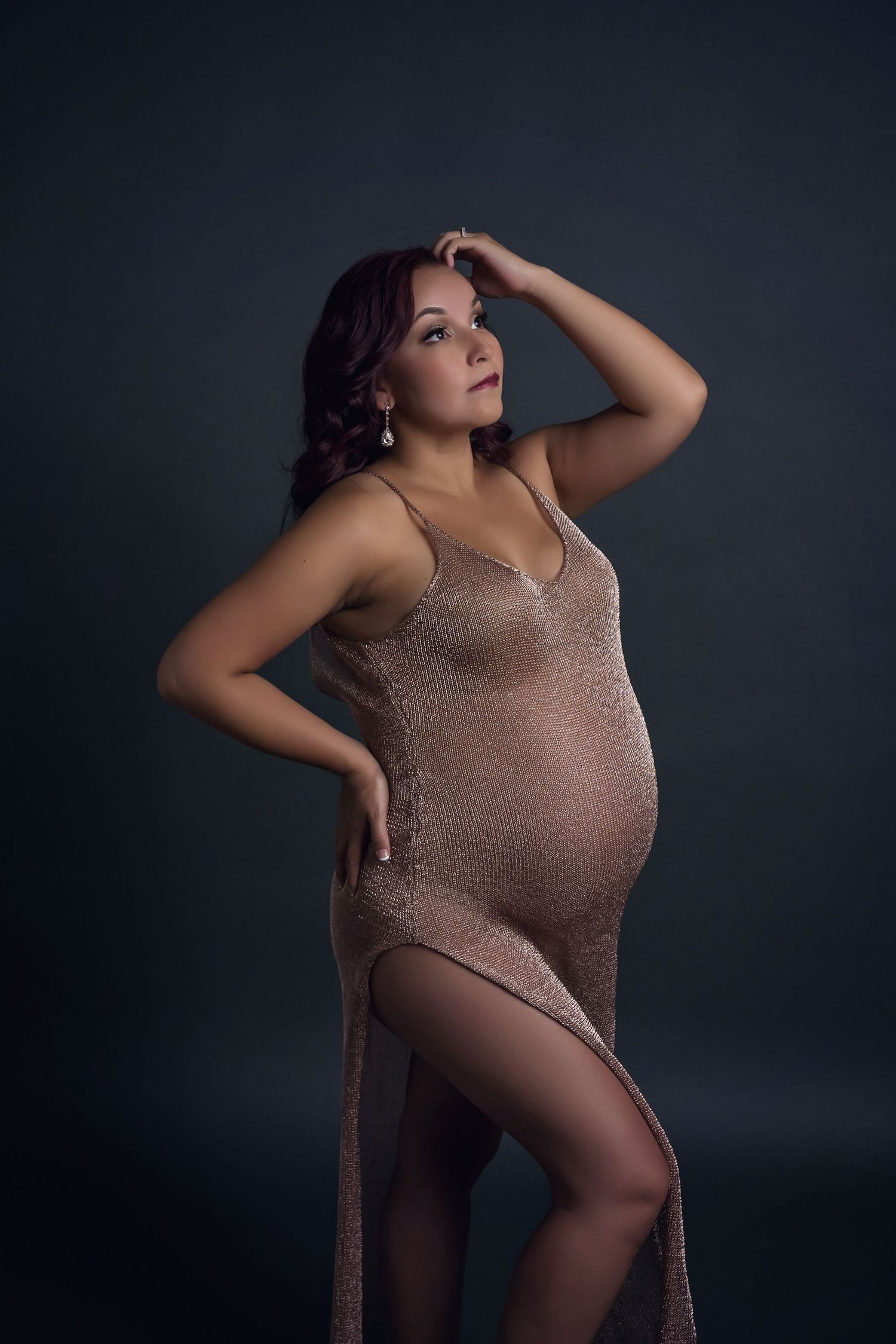 Glamorous maternity portrait in sparkly bronze gown on dark backdrop