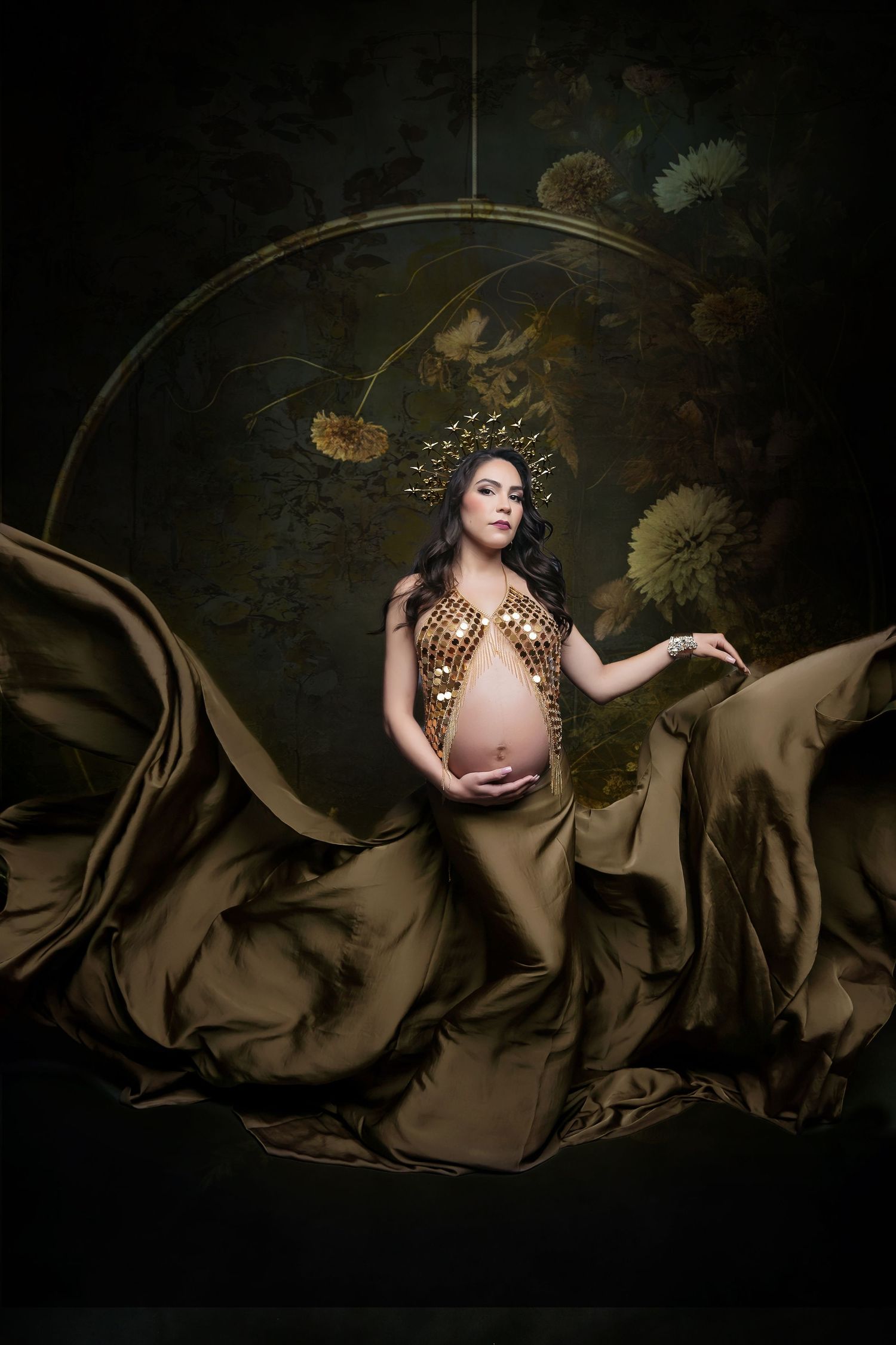 Maternity portrait with flowing satin brown fabric and gold accents on dark background