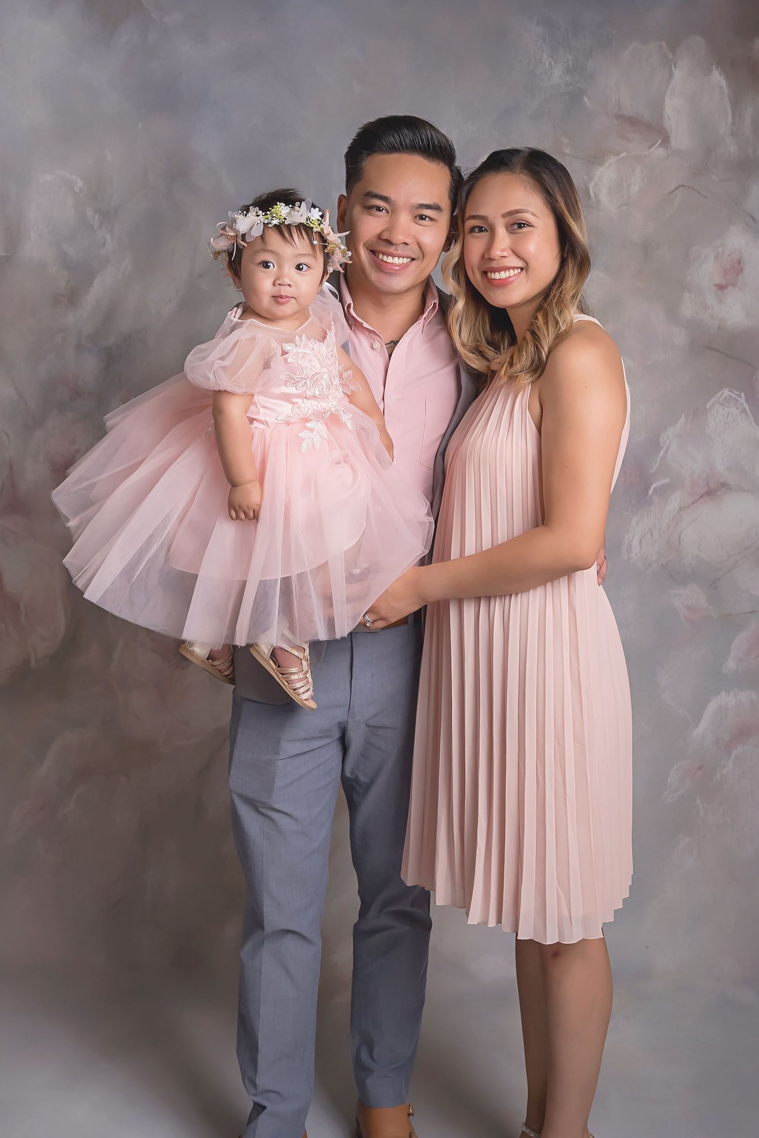 Family portrait with parents and baby in matching pink and gray clothing inside a San Diego studio
