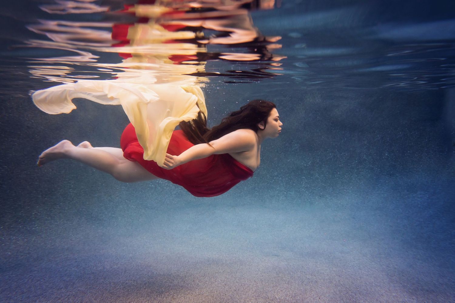 Underwater maternity image with flowing fabrics creating elegant shapes in deep blue water