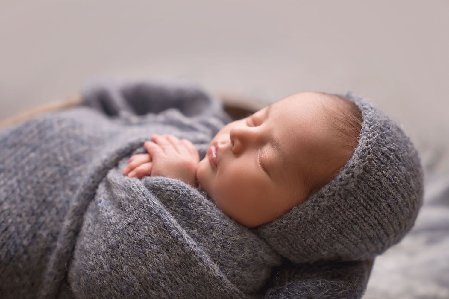 Artistic newborn photo sequence with baby sleeping in grey wrap on round wooden prop. San Diego Newborn Photographer