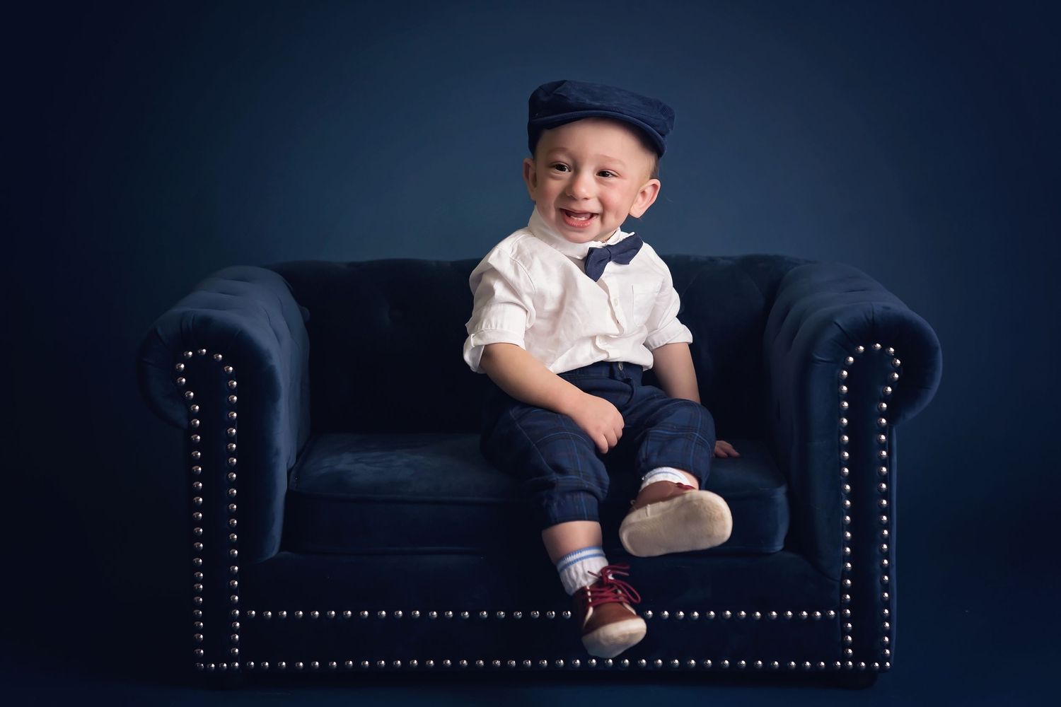 Navy studio setup featuring a classic tufted leather sofa with studded details. San Diego cake smash photographer