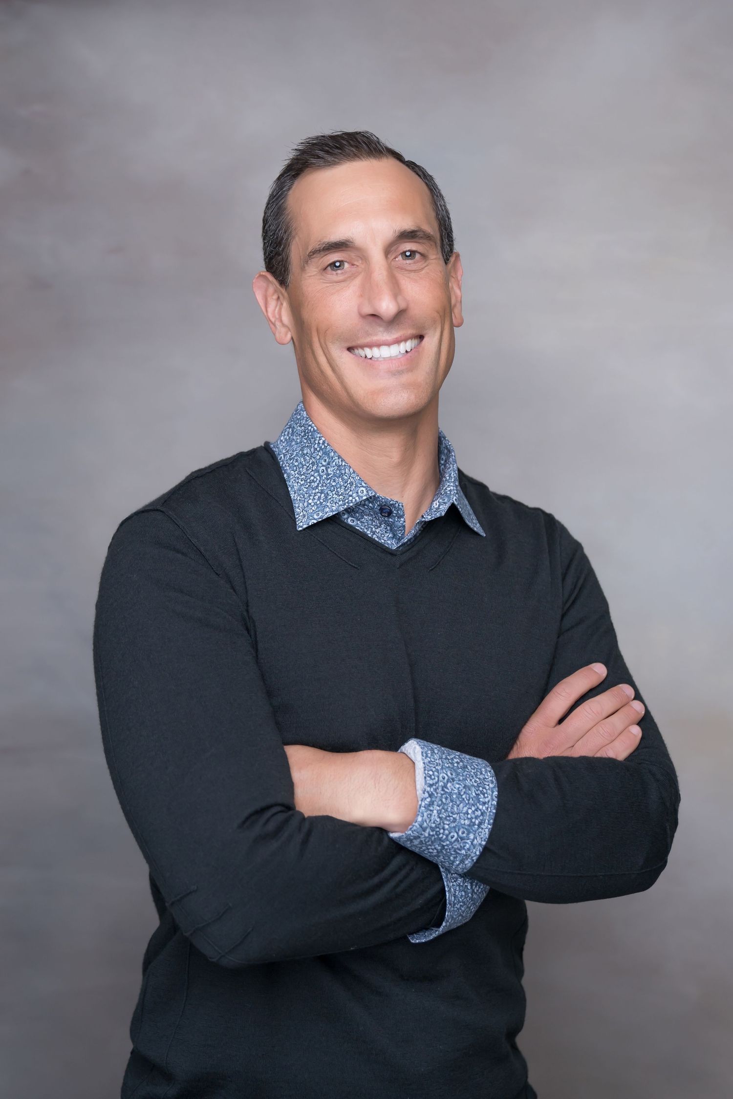 Professional portrait of man in black sweater with patterned collar posed confidently