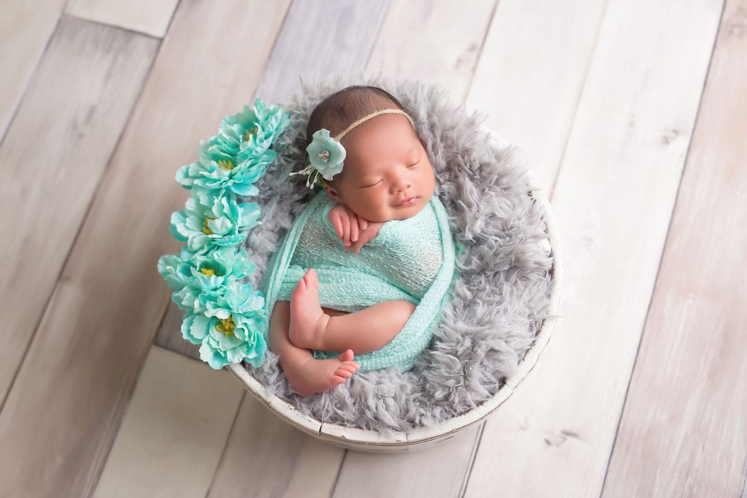 Newborn baby wearing mint green outfit resting on soft gray blanket during studio session. San Diego Newborn Photographer