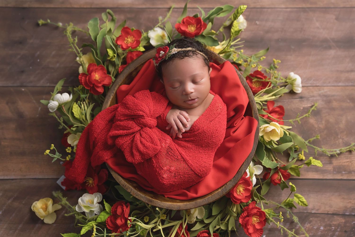 Newborn photography with red fabric and floral arrangements on wooden background. San Diego Newborn Photographer