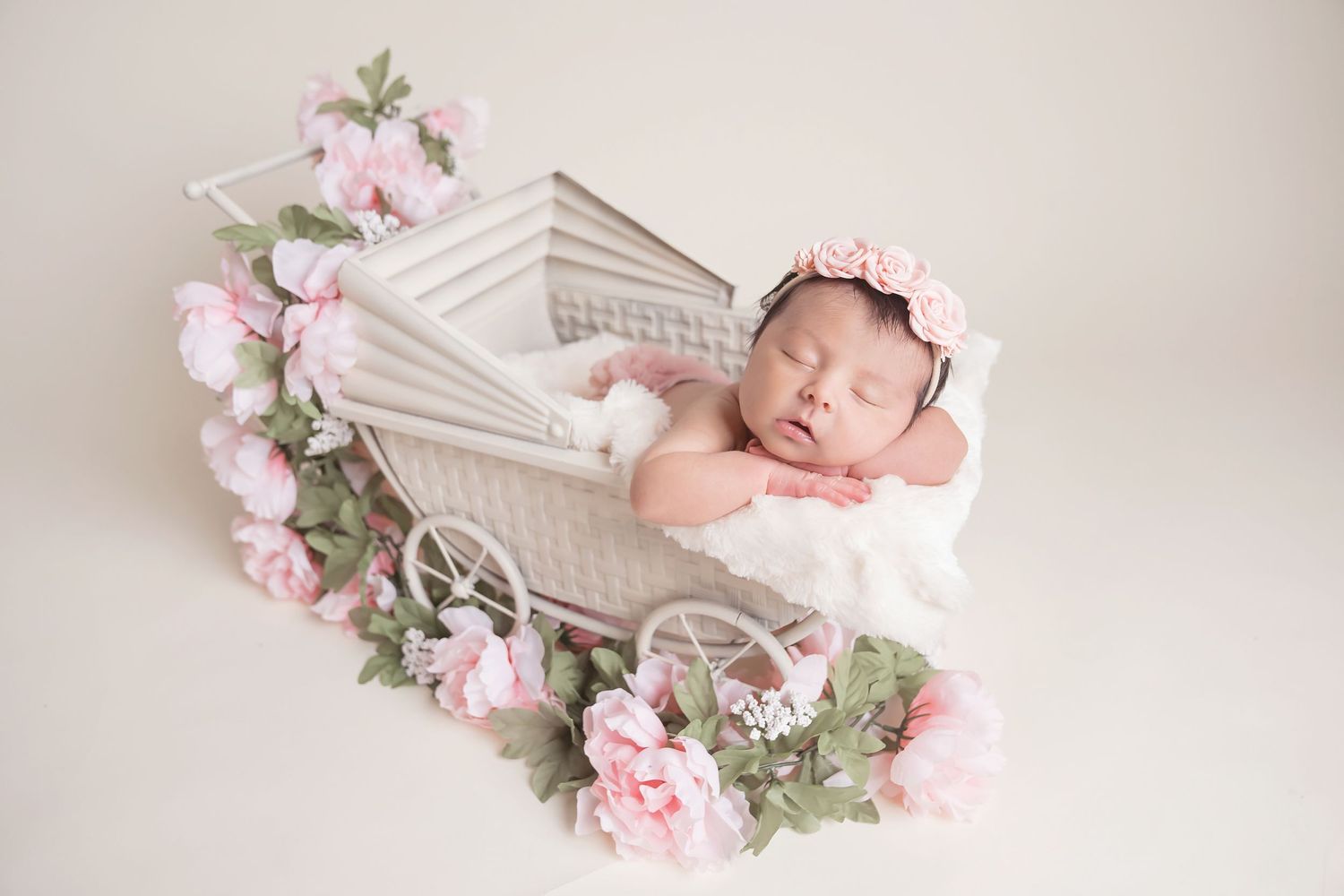 Sleeping newborn in white cart surrounded by pink floral decorations. San Diego Newborn Photographer