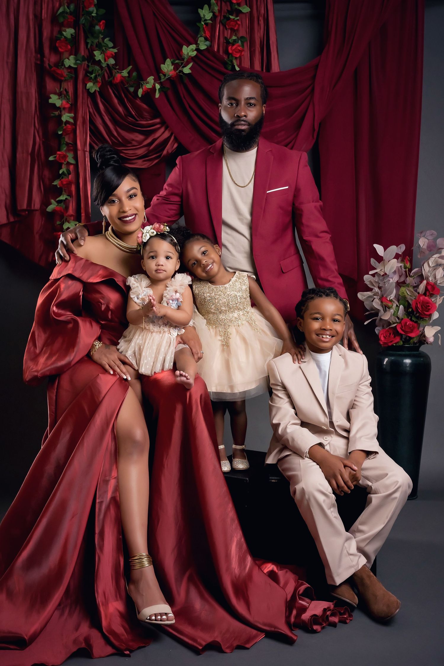 Elegant family portrait with coordinated cream outfits and burgundy drapes in a formal studio setting