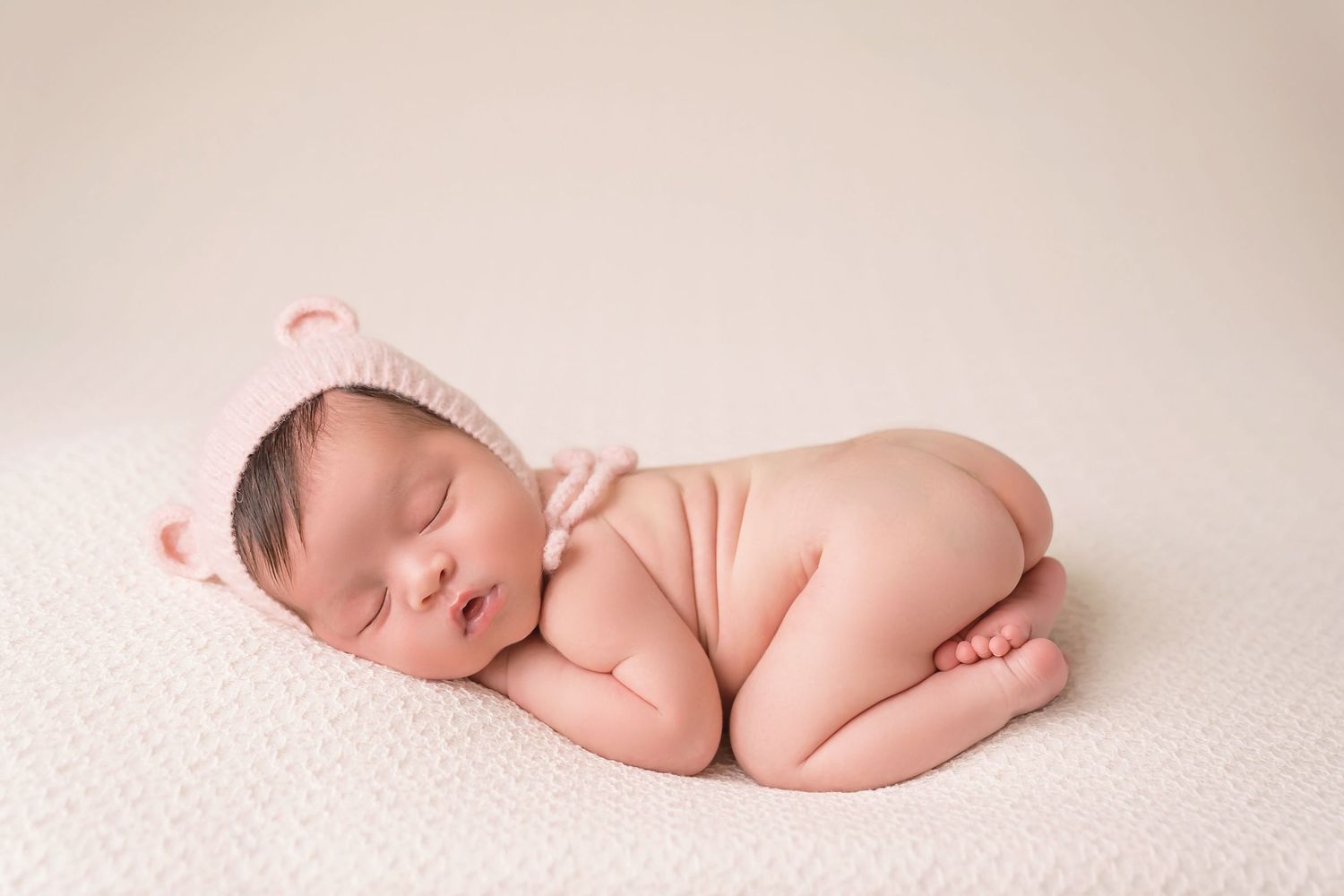 Simple minimalist newborn photography on cream textured backdrop with soft natural lighting. San Diego Newborn Photographer