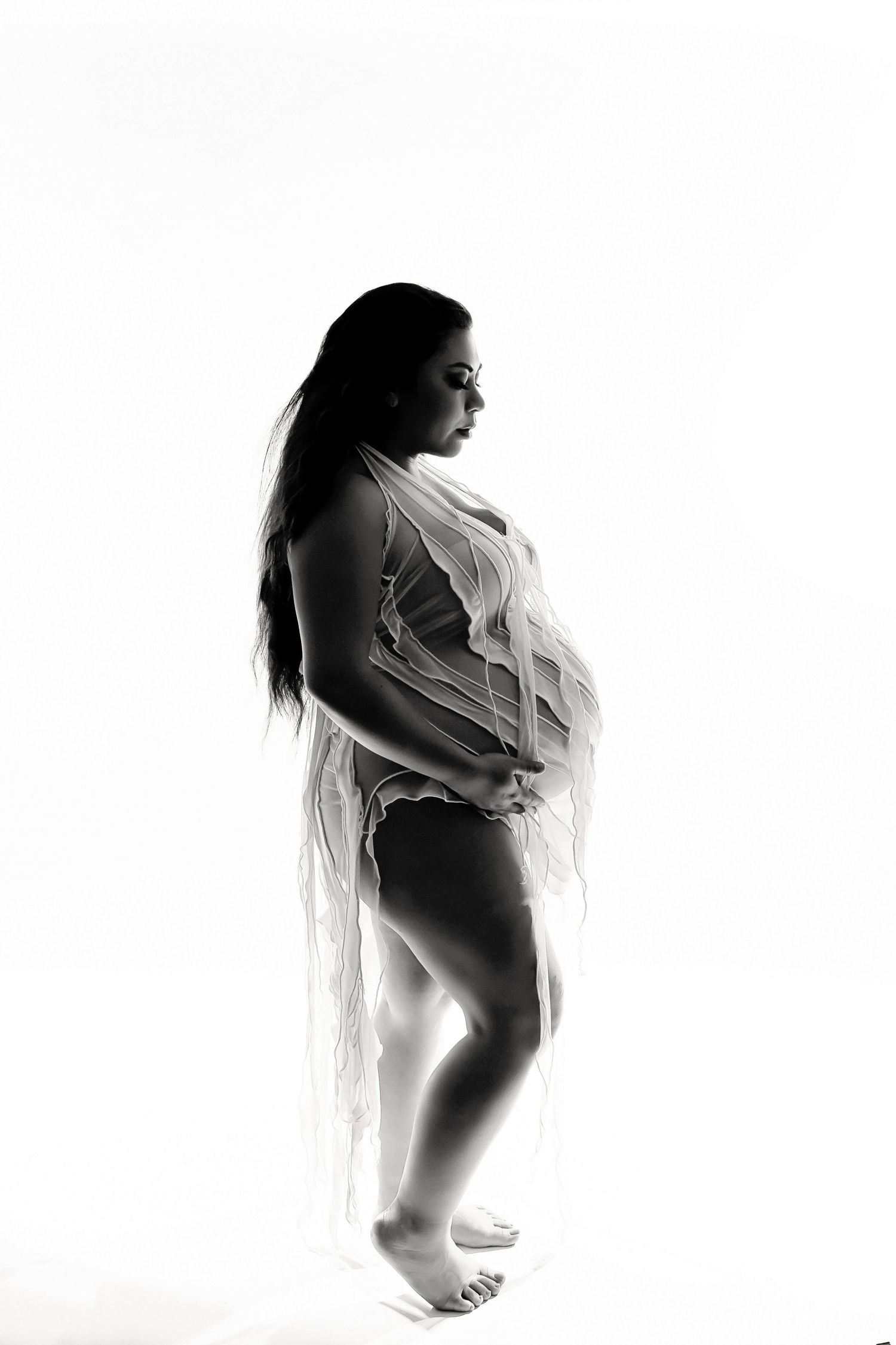 High-key maternity silhouette with delicate white fabric creating an ethereal effect