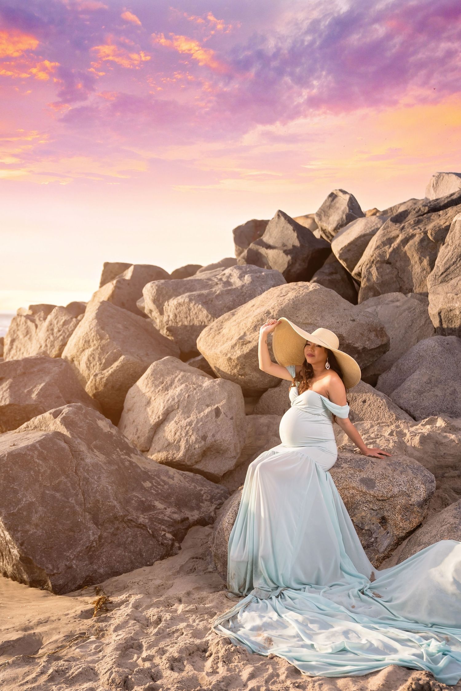 Romantic coastal maternity photography featuring flowing blue dress against rocky beach backdrop.San Diego Maternity Photographer