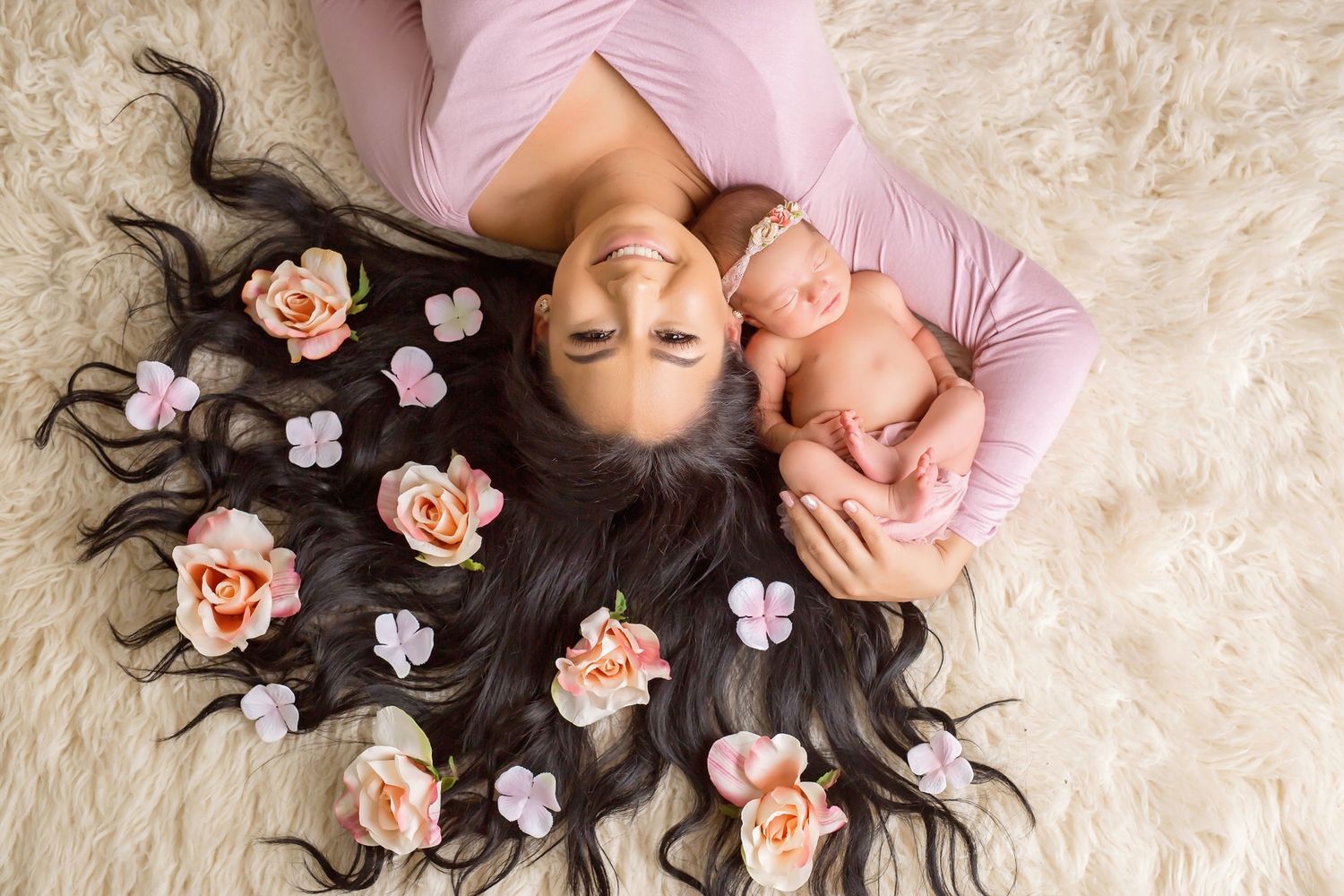 Mother and baby lying on cream carpet with scattered pink flowers during portrait session. San Diego Newborn Photographer