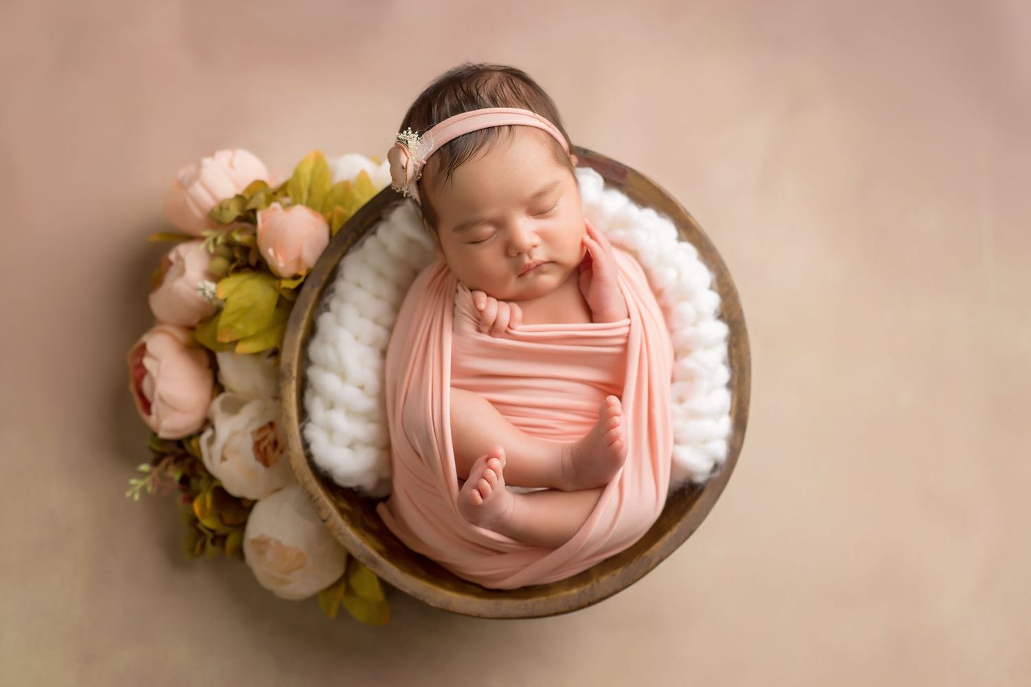 Newborn baby sleeping in vintage bowl surrounded by soft pink flowers and greenery. San Diego Newborn Photographer