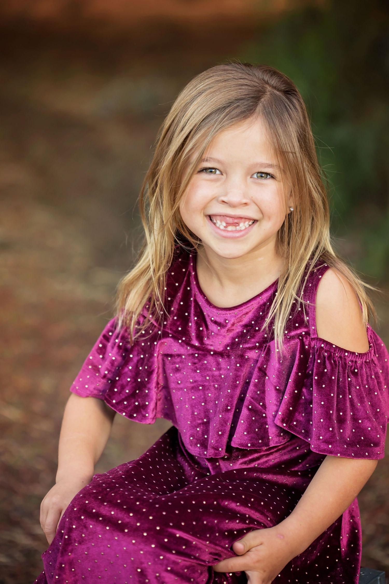 Child in a sparkly purple dress posing playfully outdoors against a rustic backdrop