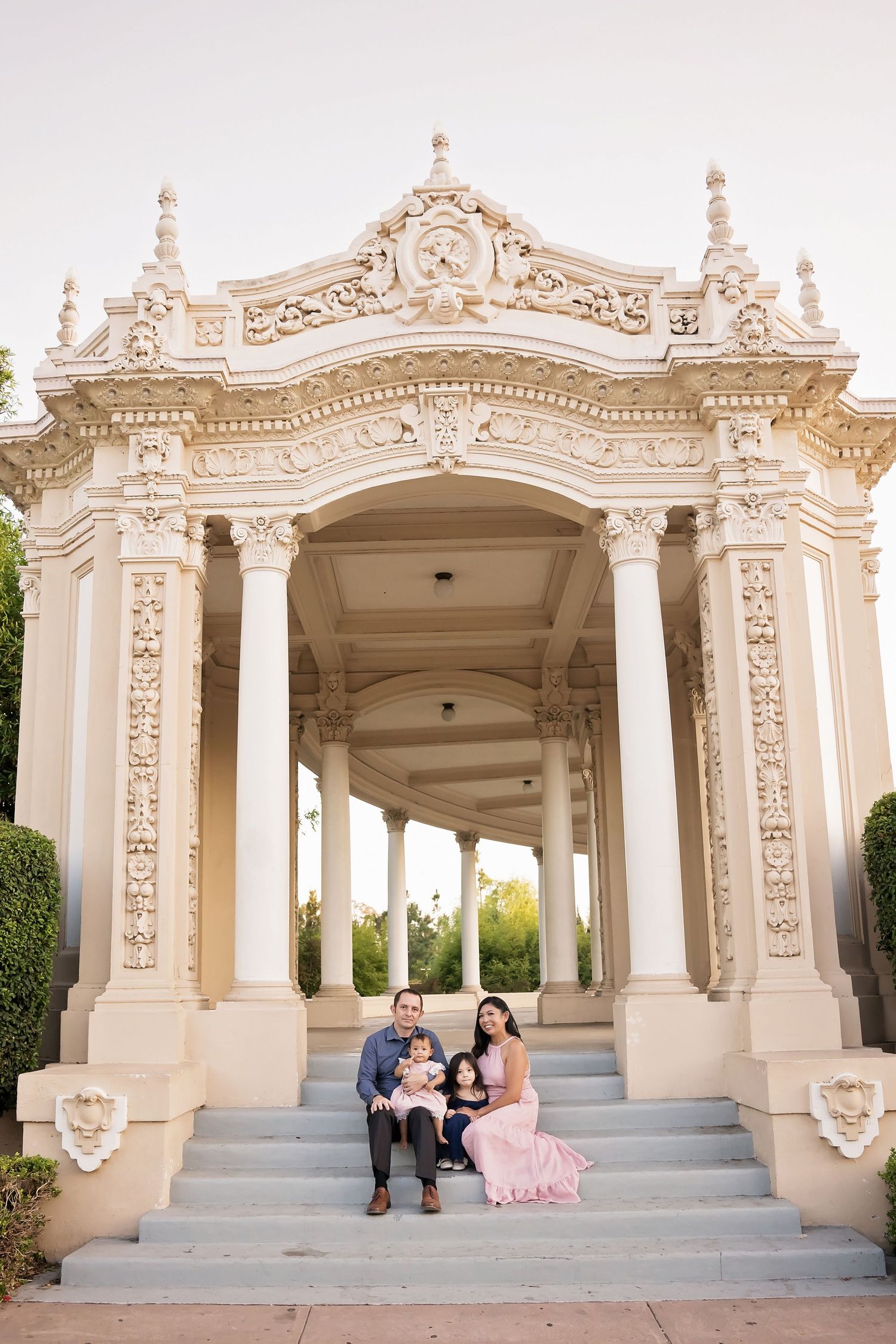Family dressed in formal attire seated on ornate white stone architectural arch and steps — San Diego family portrait