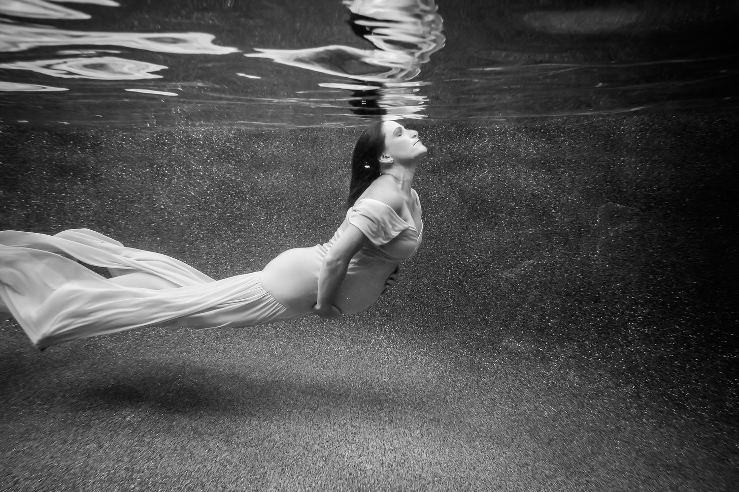 Dramatic black and white underwater maternity portrait with billowing fabric