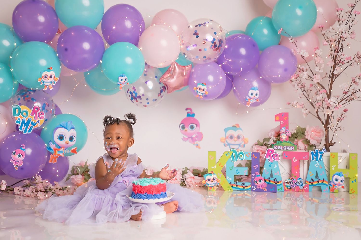 Colorful balloon arch with purple and teal balloons decorates a birthday party setup with cute plush toys.