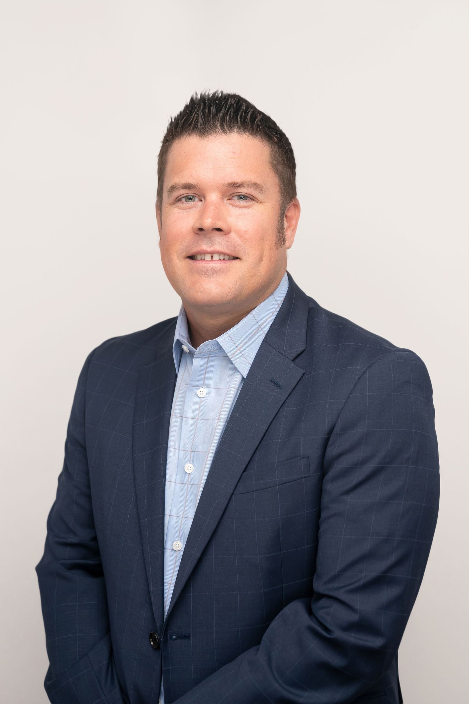 Corporate headshot of man in navy suit and blue dress shirt against clean white background