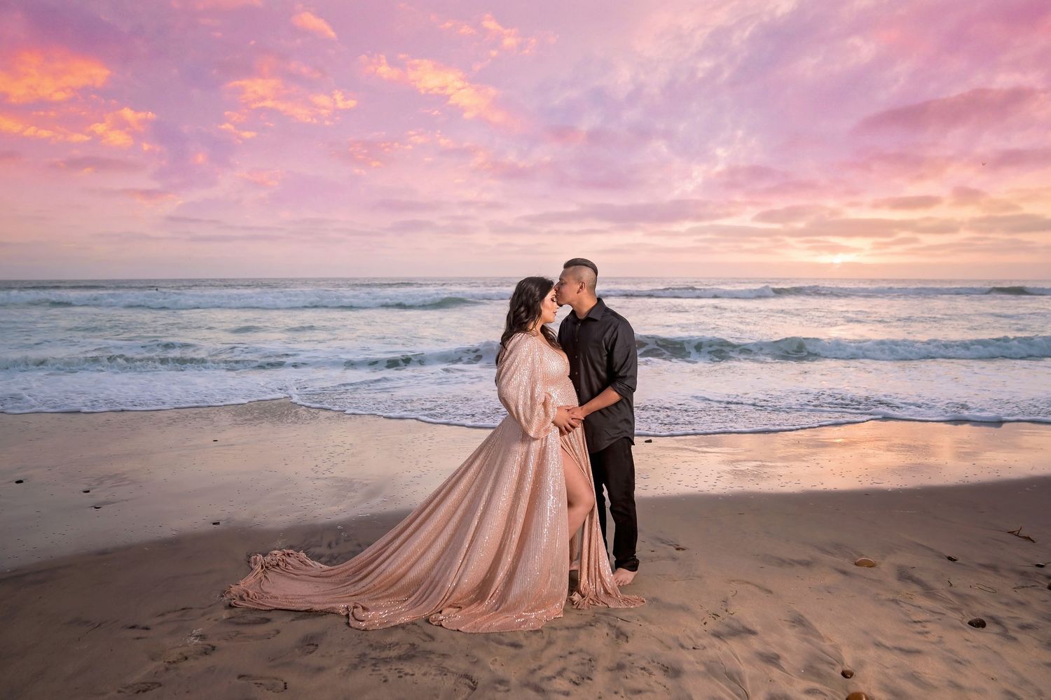 Elegant maternity beach photo session with blush gown against dramatic coastal sunset. San Diego Maternity Photographer