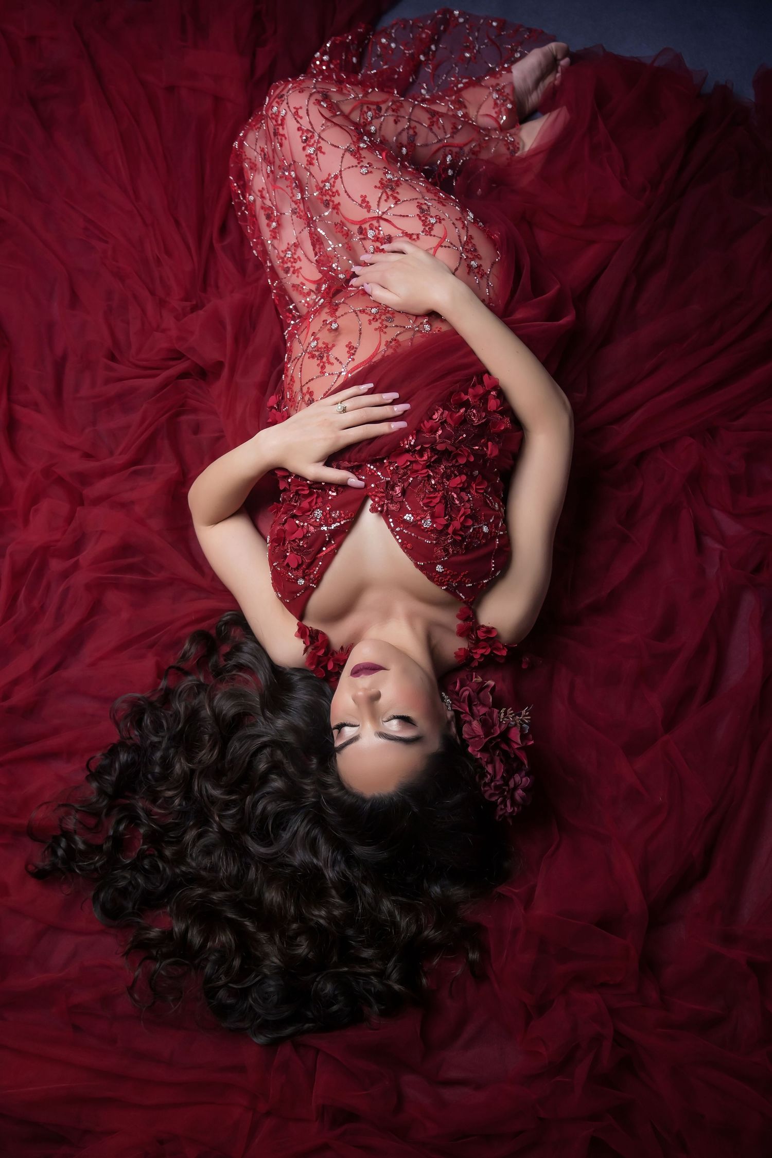 Dramatic maternity portrait series on deep red fabric featuring a sparkly burgundy dress in san diego photography studio.
