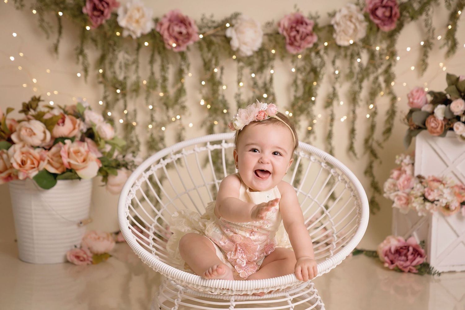 White wicker chair decorated with pink roses and floral garlands for a baby photoshoot. San Diego cake smash photographer