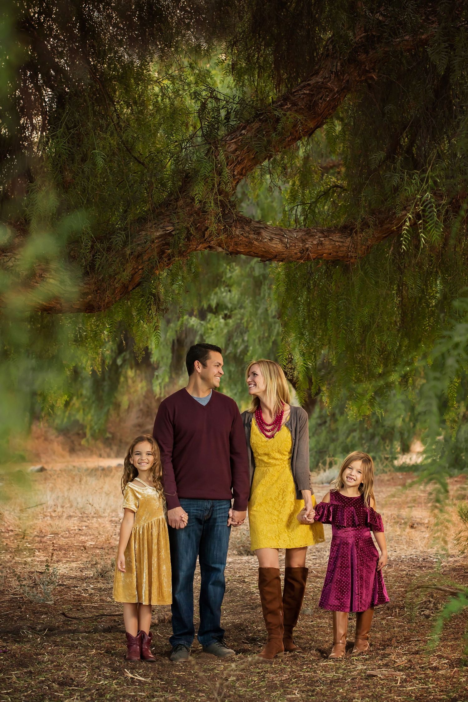 Family walking together under trees wearing coordinated fall colors of yellow and burgundy.