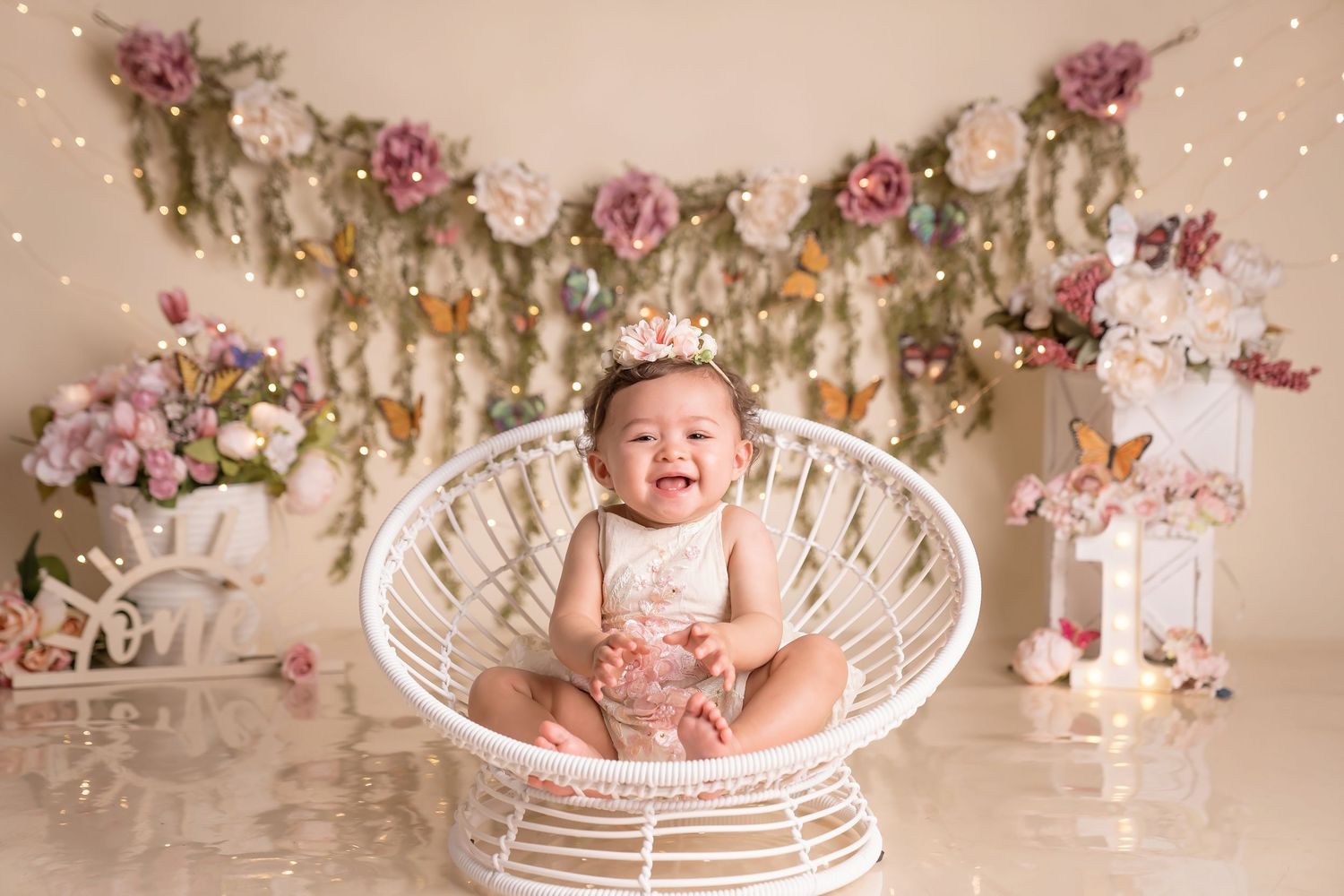 Cake smash photography session with Floral decorated backdrop, hanging lights, and white wicker chair for a photo session.