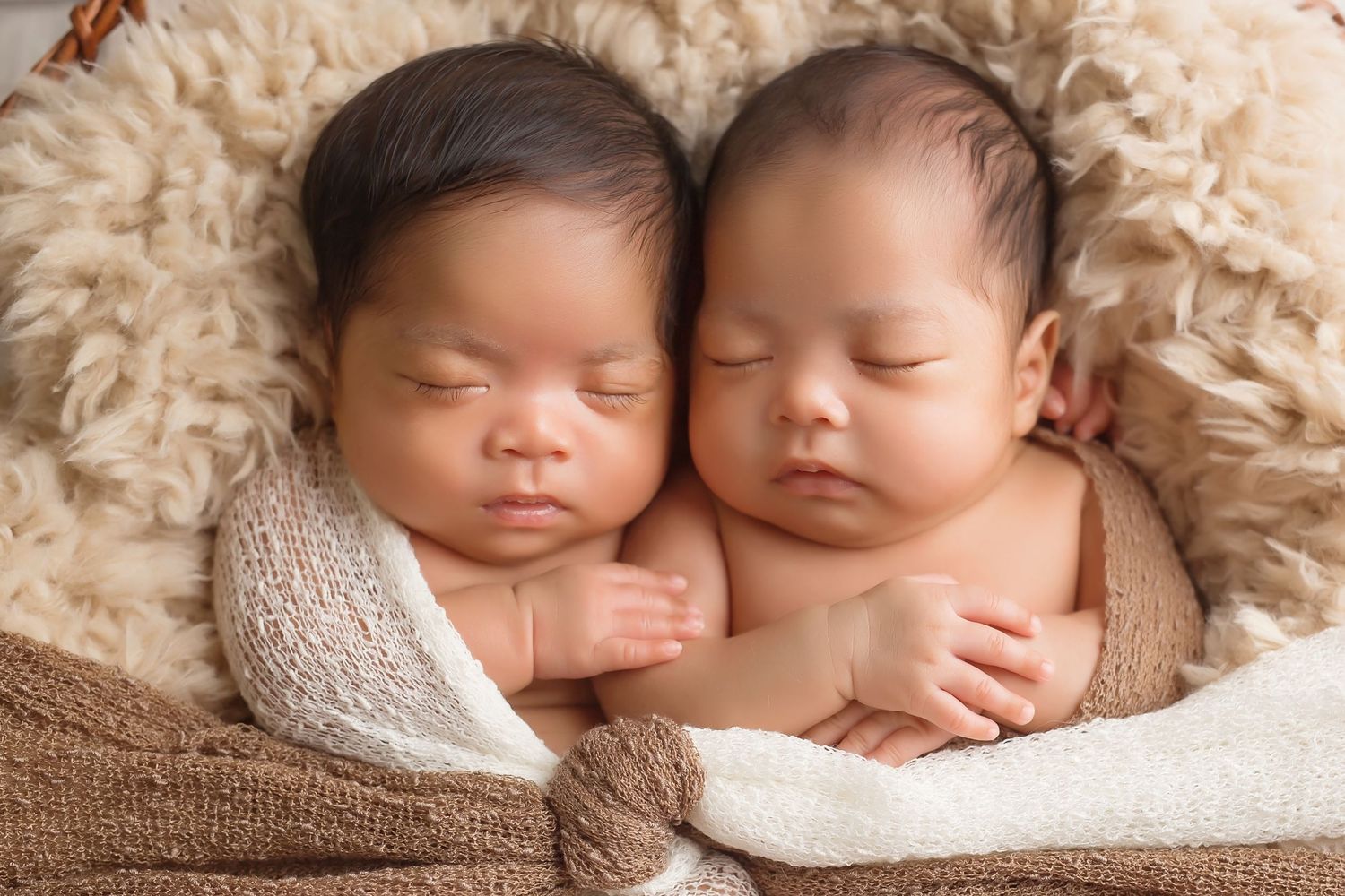 Twin newborns sleeping peacefully together on textured brown blanket during portrait session. San Diego Newborn Photographer
