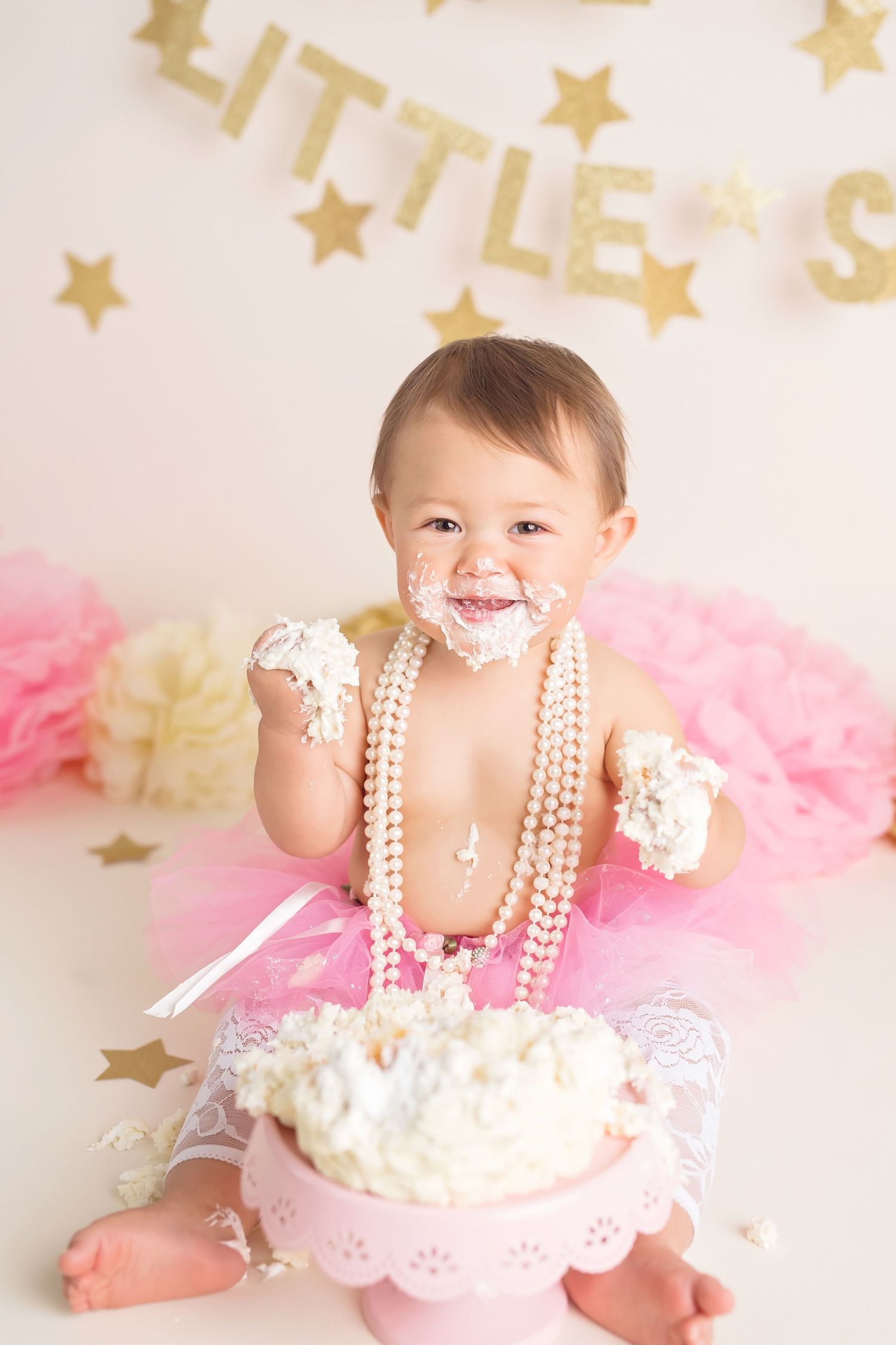 Festive first birthday cake smash session with pearls, pink tulle, and gold star decorations. San Diego cake smash photographer