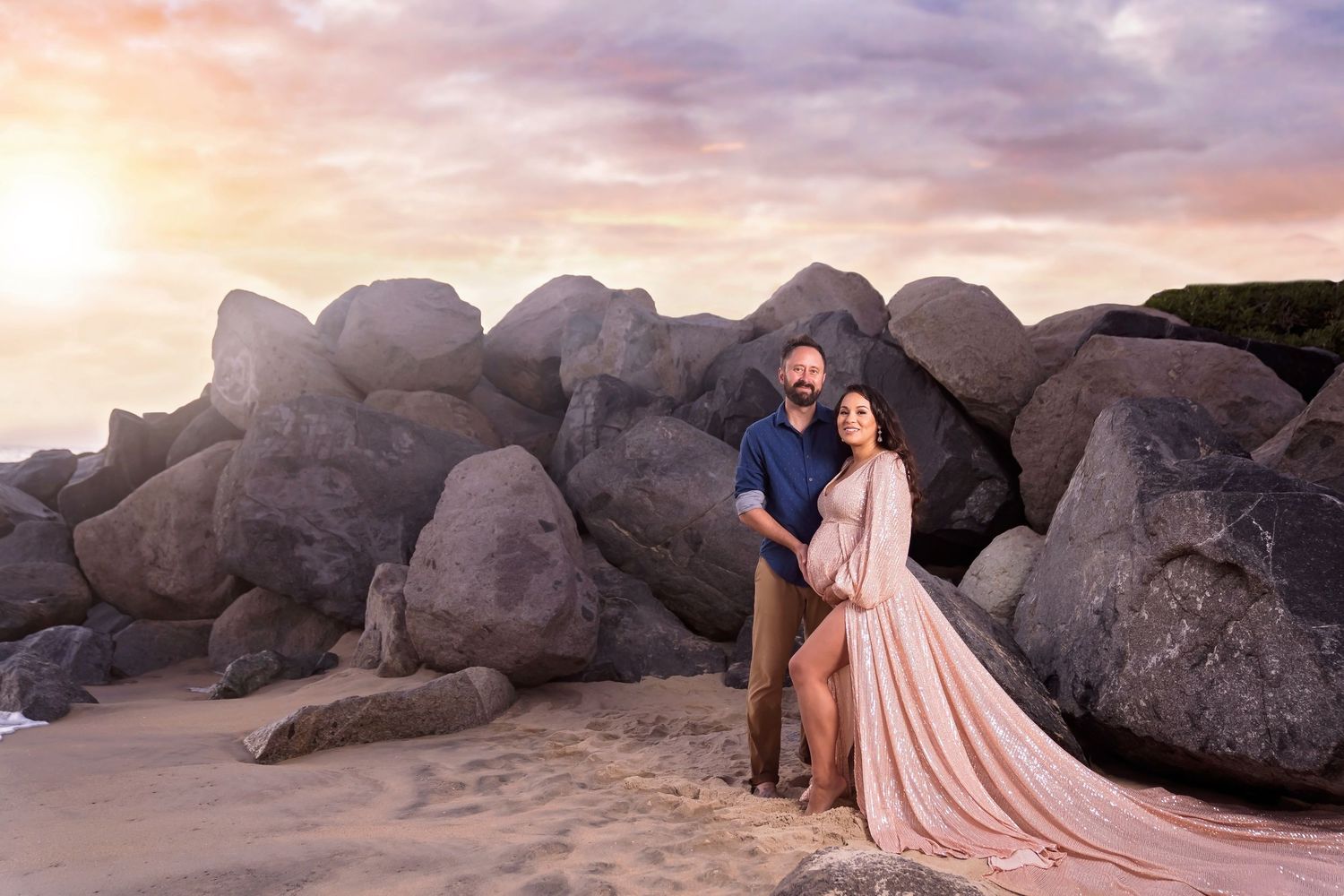 A pregnant  couple poses against rocky coastal backdrop in coordinated formal attire at sunset. San Diego Maternity Photographer
