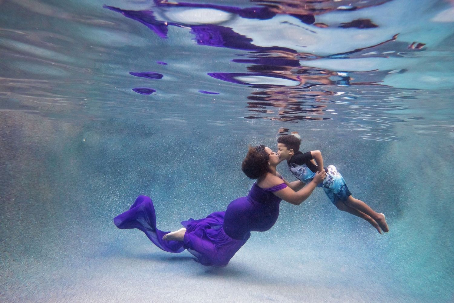Underwater maternity portrait with purple fabric drifting elegantly in blue water