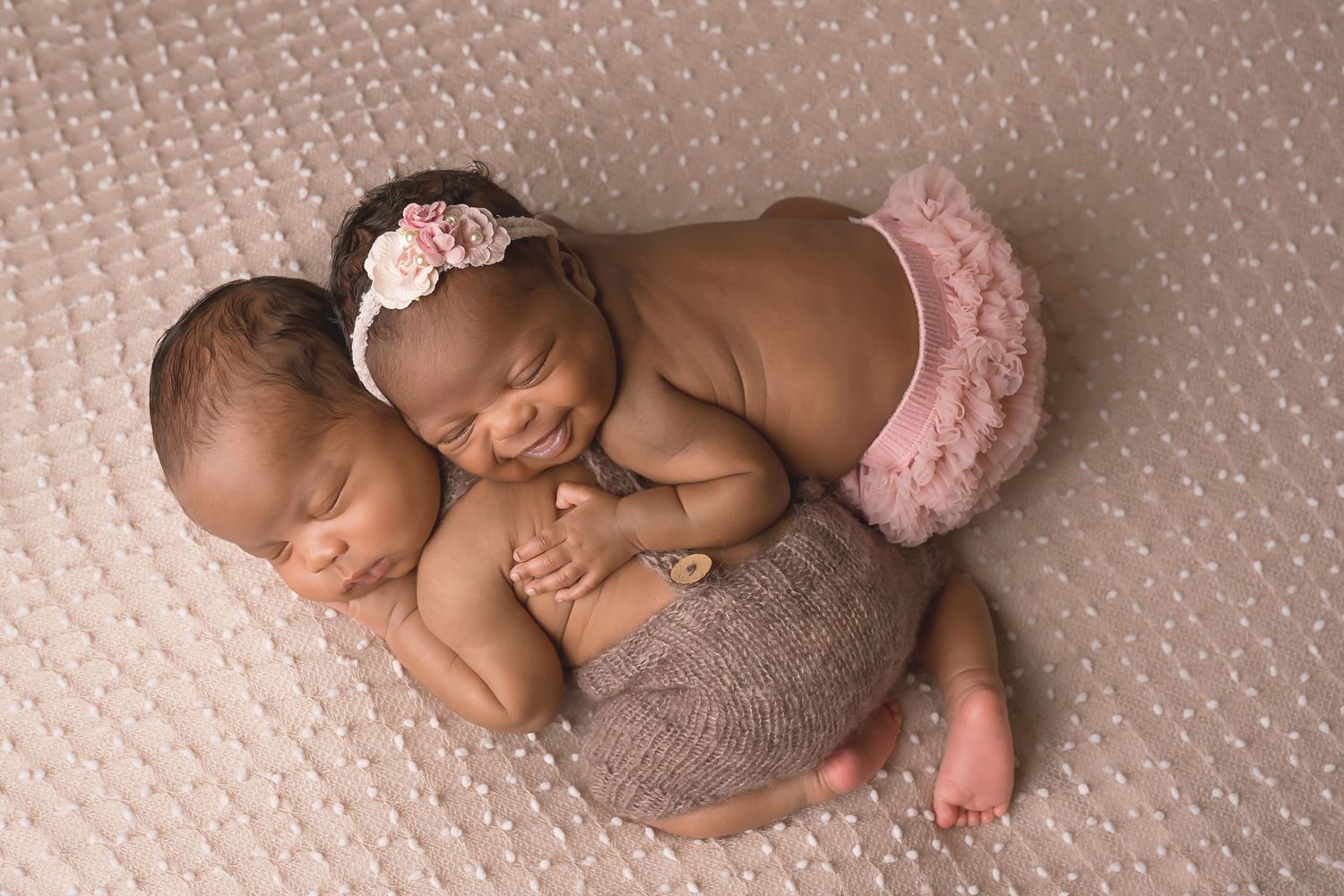 San Diego newborn photographer captures Newborn twins resting together on textured beige backdrop.