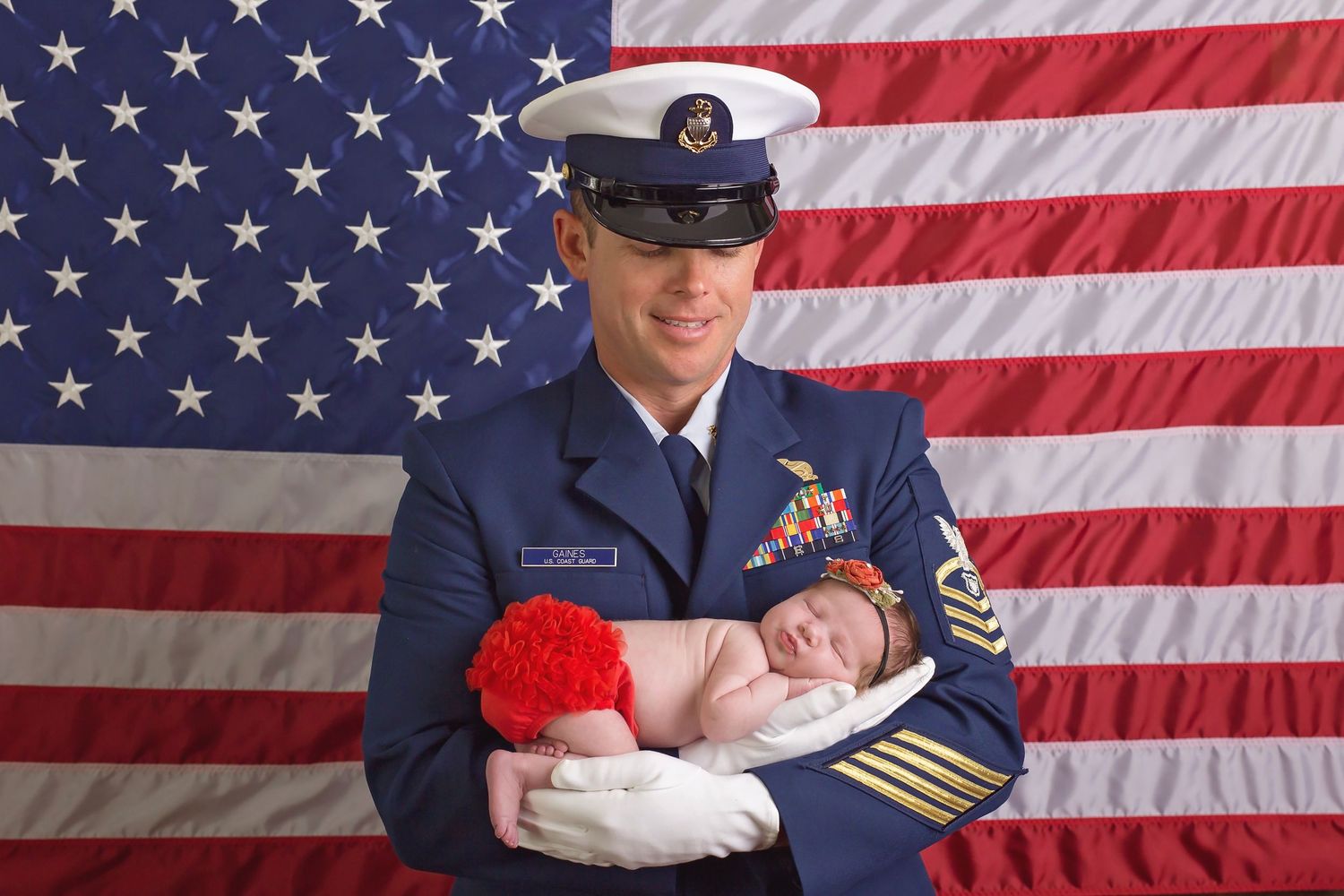 Military personnel in uniform holding newborns against American flag backdrop. San Diego Newborn Photographer
