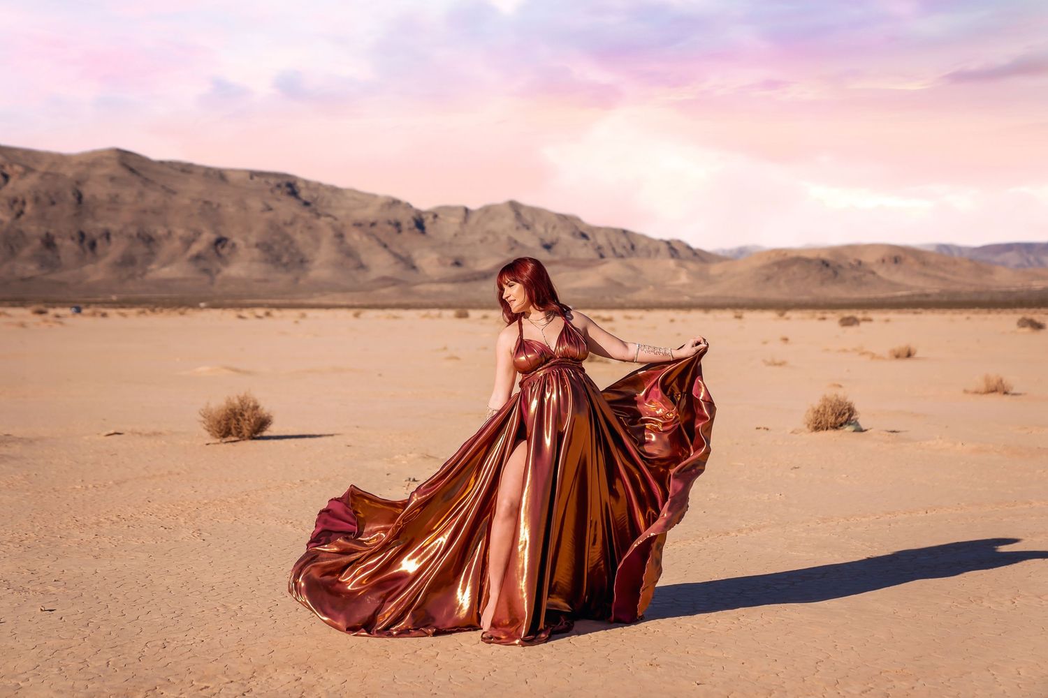 Burgundy gown billows dramatically across desert floor with mountains in background. San Diego Maternity Photographer