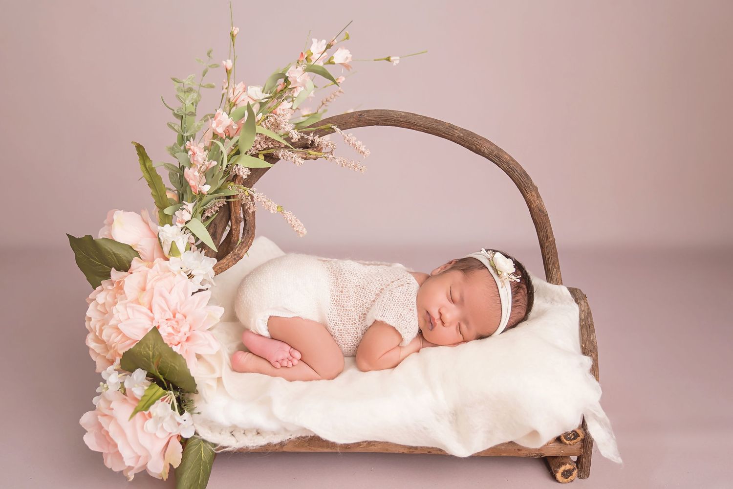 Artistic newborn portrait setup with curved wooden prop and pink floral accents. San Diego Newborn Photographer