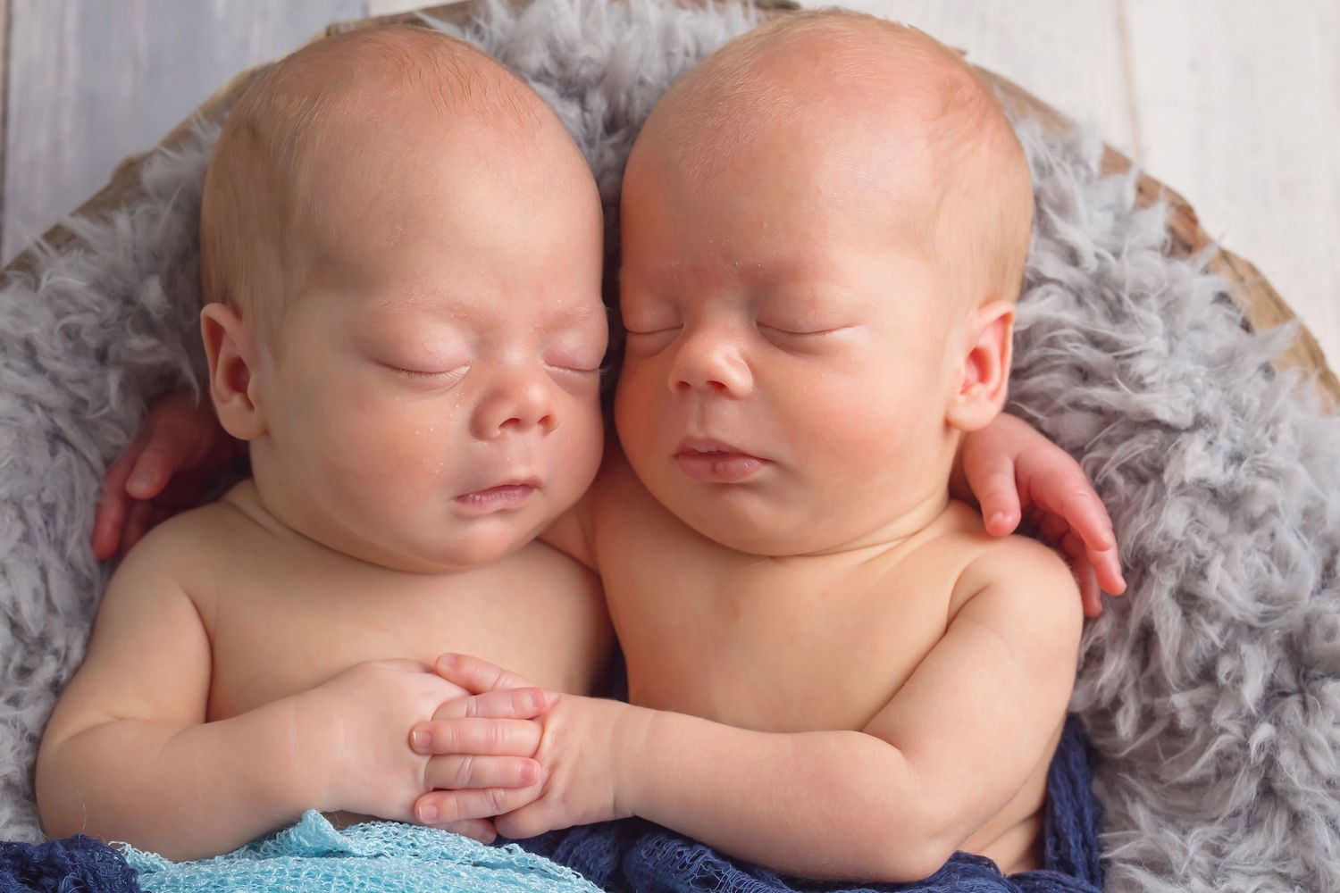 Twin babies sleeping side by side on soft grey blanket during newborn photoshoot. San Diego Newborn Photographer