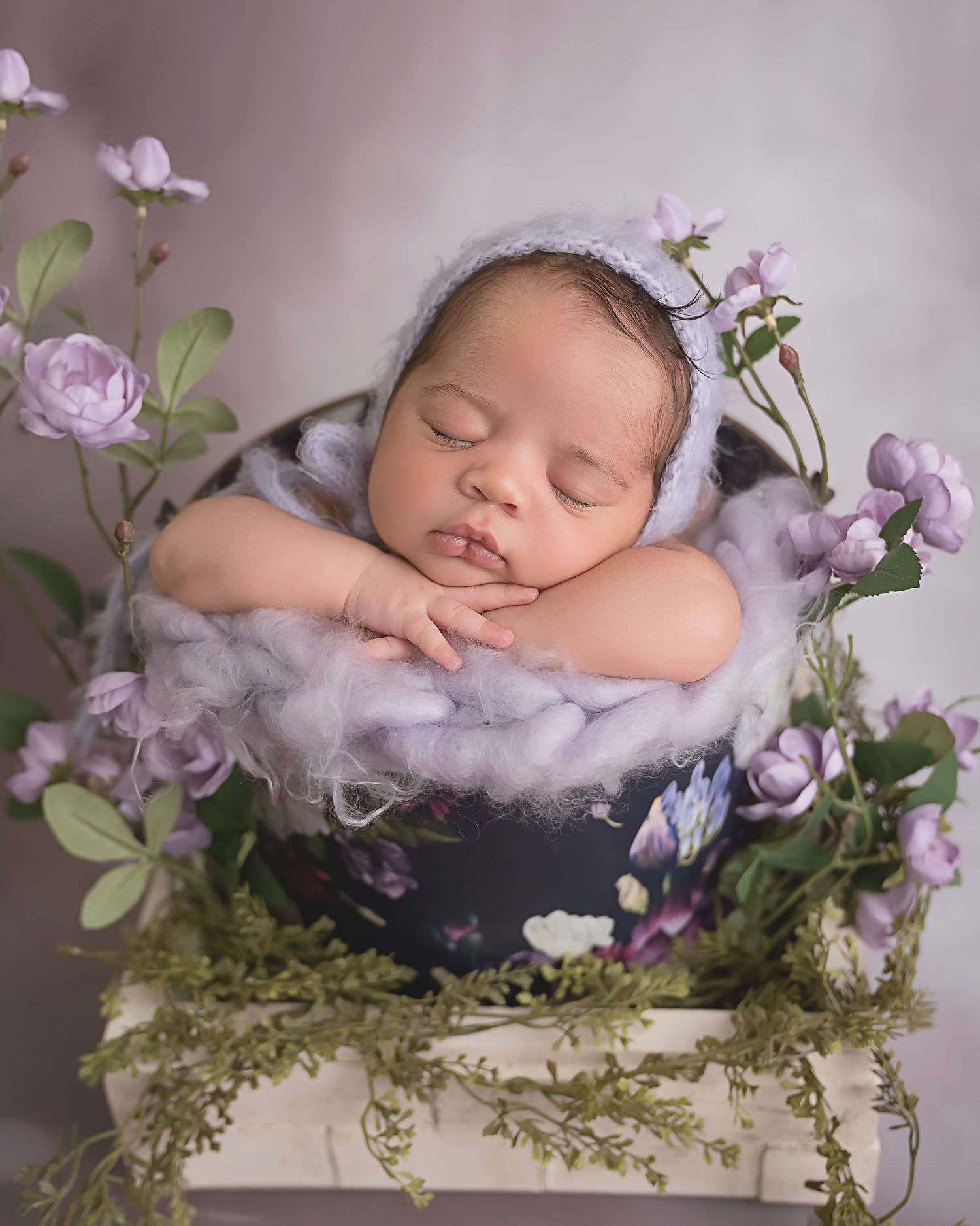 San Diego newborn photographer captures Newborn in navy wrap surrounded by purple flowers and greenery in artistic composition.