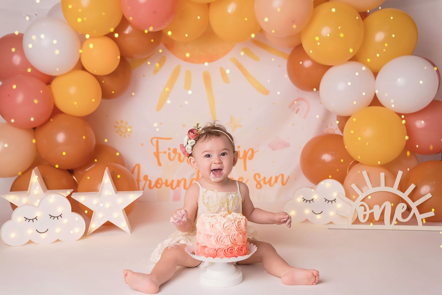 Whimsical orange and pink balloon arch with sun and star decorations.